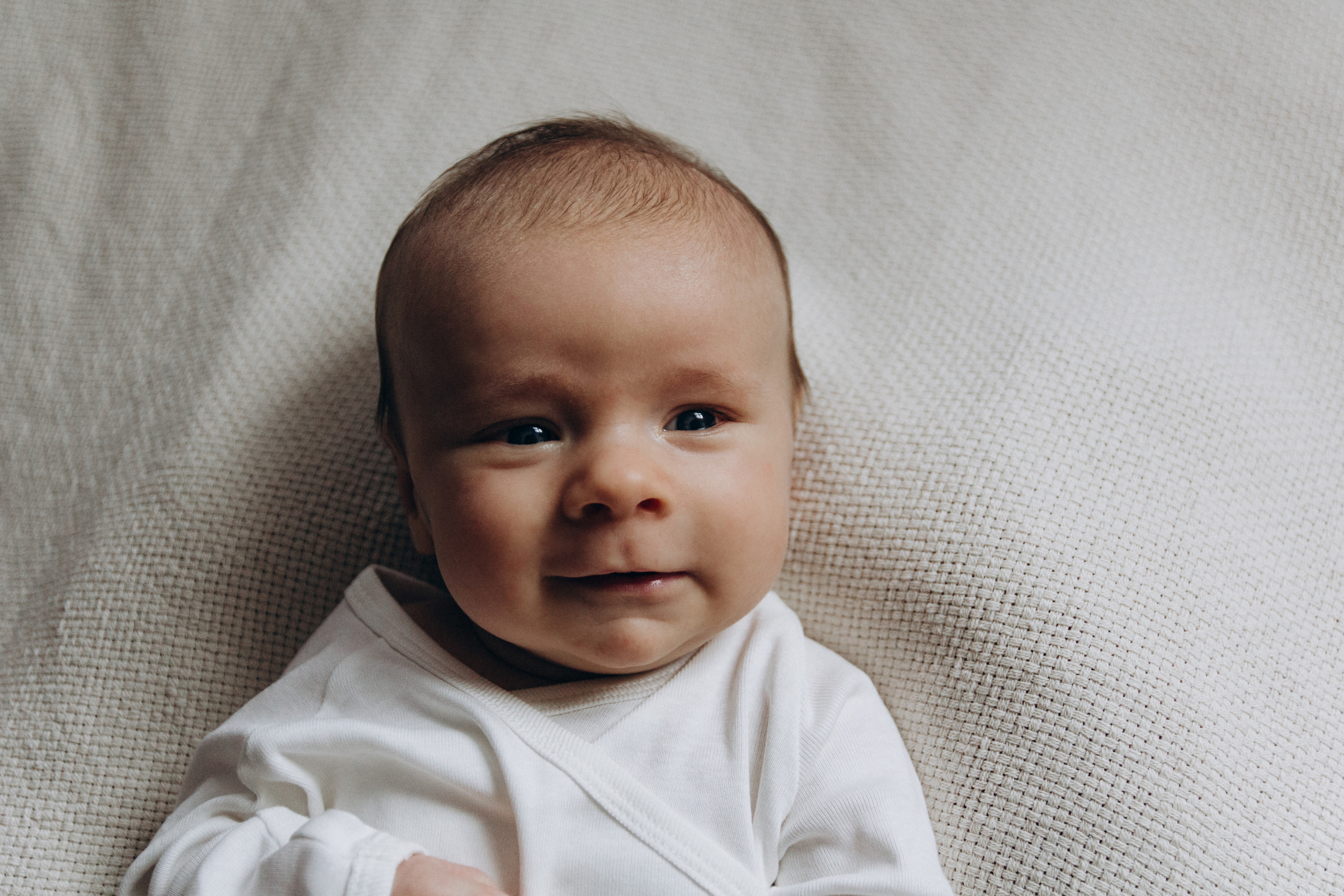 Neugeborenes Baby auf einer hellen Decke – liebevolle und natürliche Babyfotografie im Rahmen einer Newborn Session zu Hause.