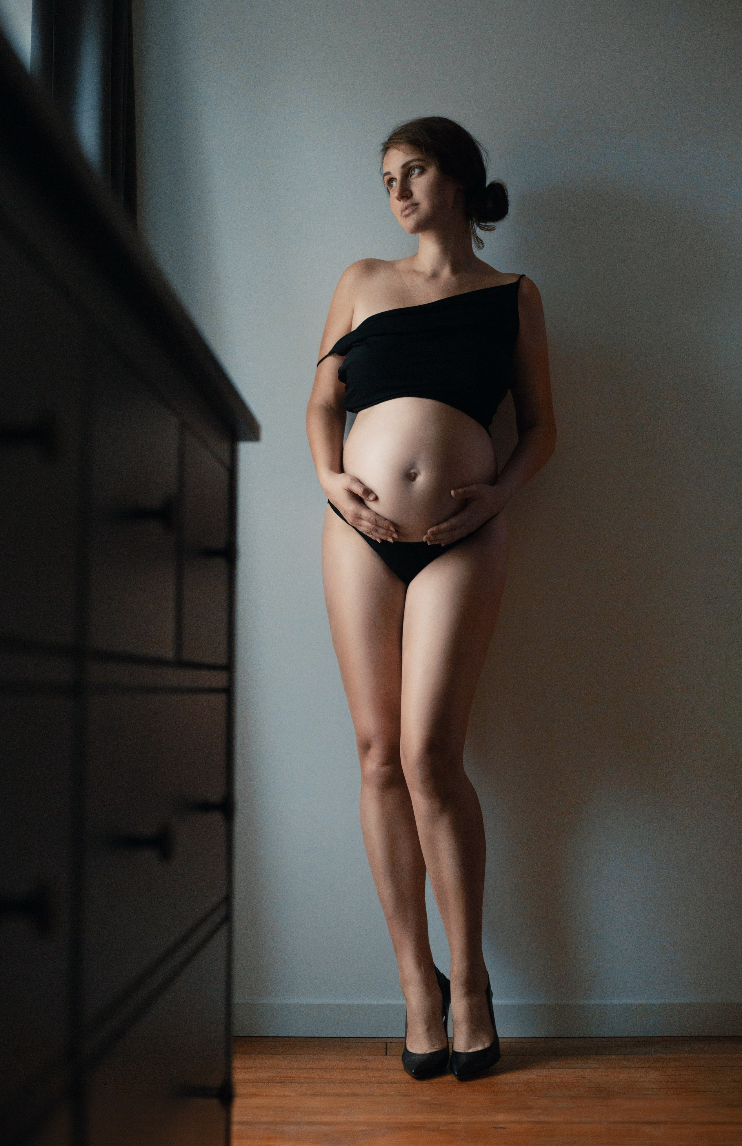 Portrait artistique d'une femme enceinte en lingerie noire, debout avec élégance près du mur