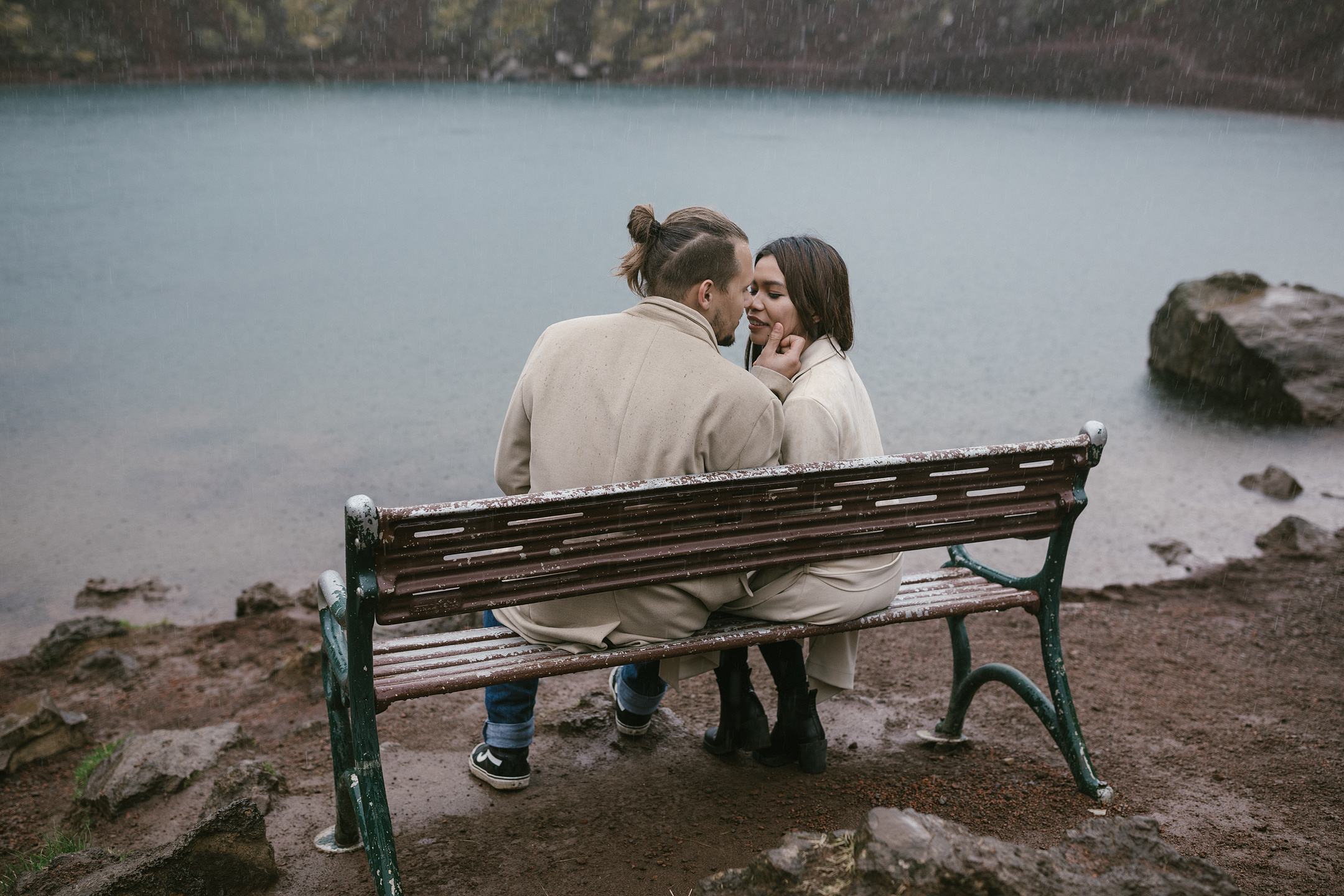 Engagement photo session on bench in rain by Iceland crater lake