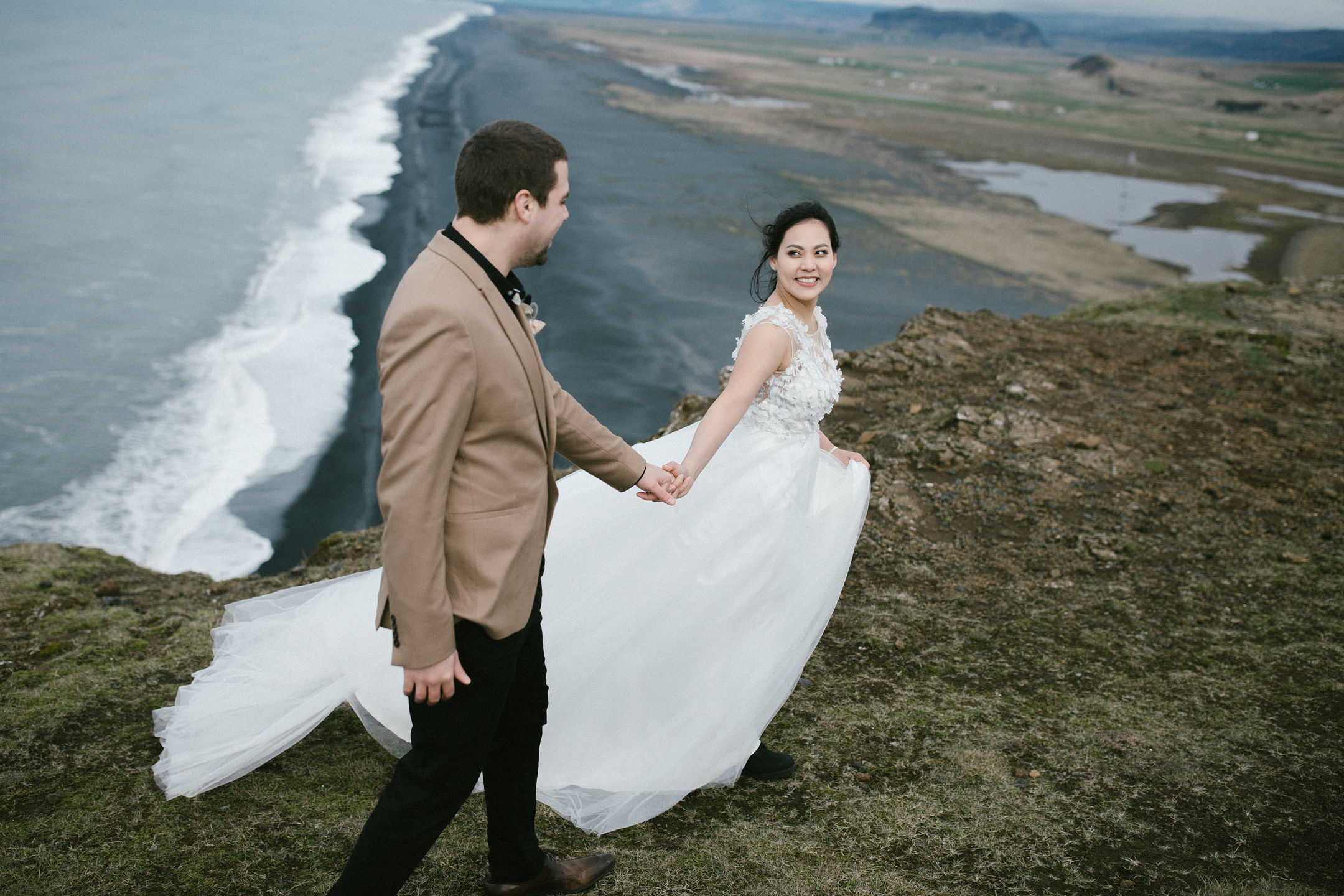 Braut führt Bräutigam entlang der Klippen von Dyrhólaey
