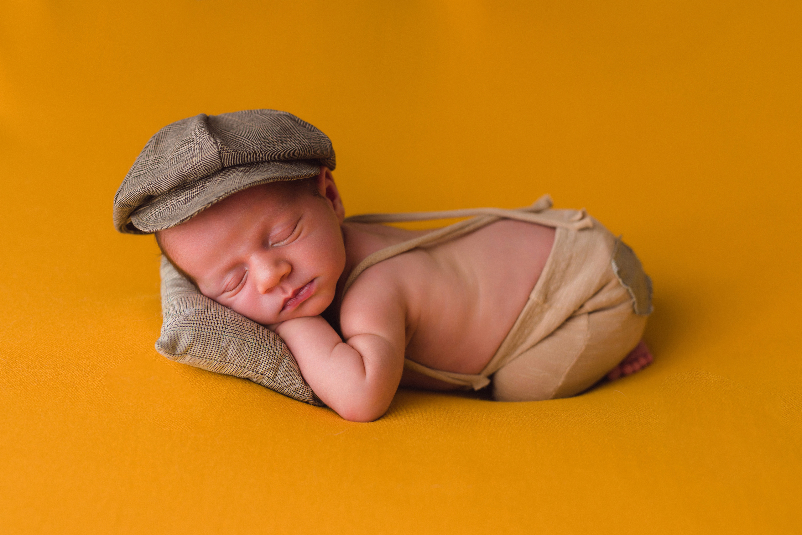 Babyfotografie zuhause – Neugeborener mit Mütze auf gelbem Hintergrund
