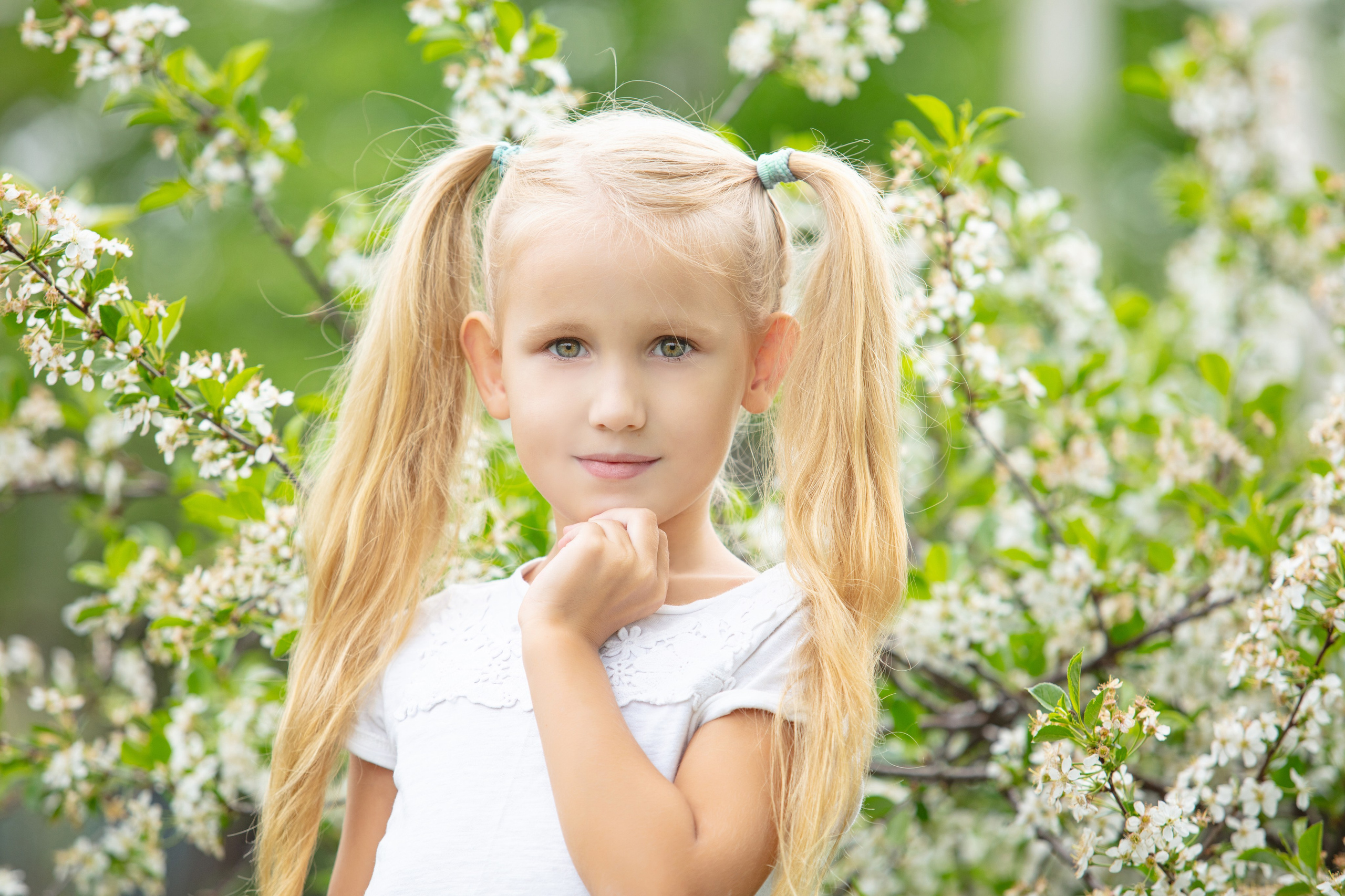 Portrait d'une petite fille blonde en robe blanche dans un jardin fleuri au printemps