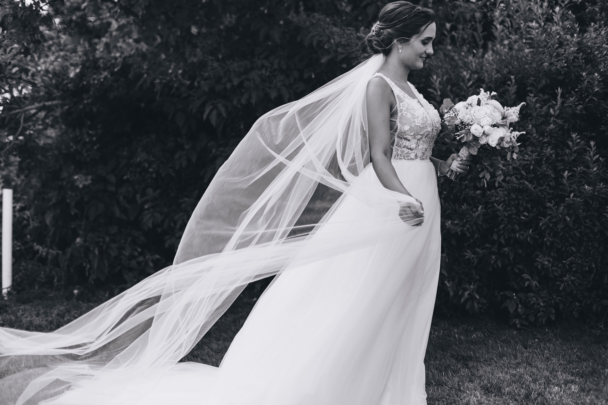 Der Schleier der Braut weht im Wind, während sie ihren Hochzeitsstrauß betrachtet.