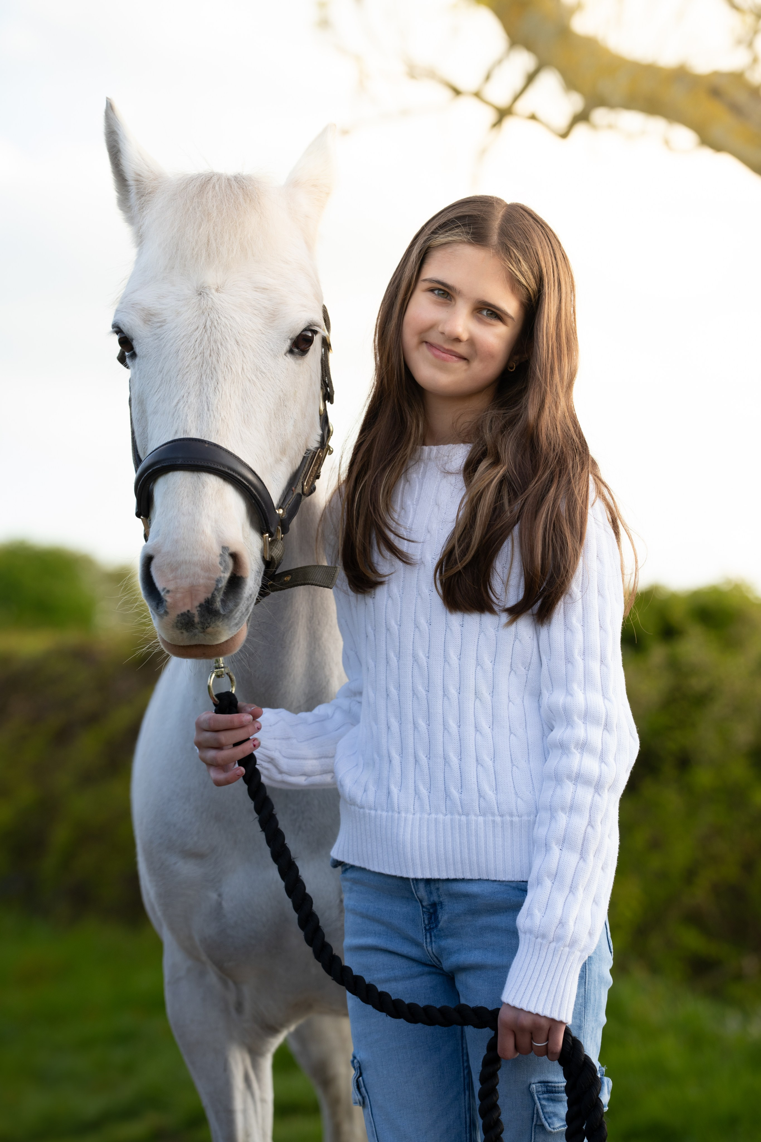 Happy girl holding reins of her pony during golden light portrait session