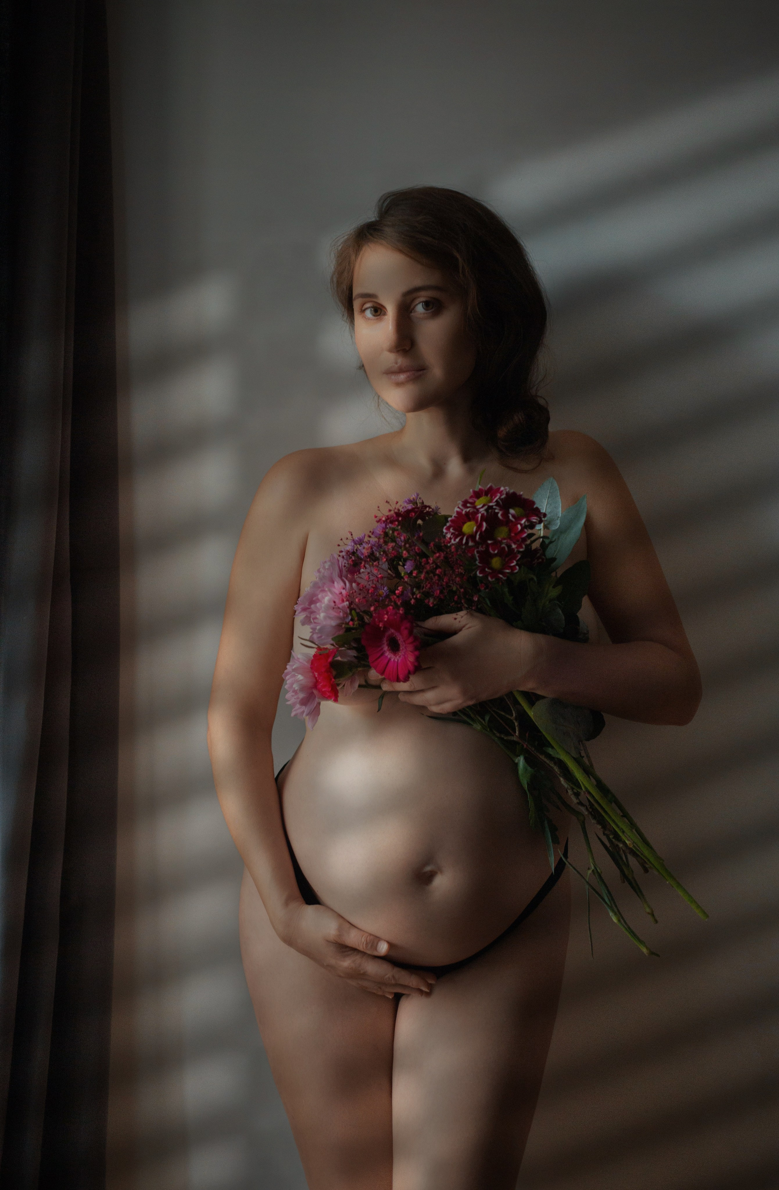 Portrait artistique de grossesse, femme enceinte avec fleurs et jeu d’ombres sur le corps
