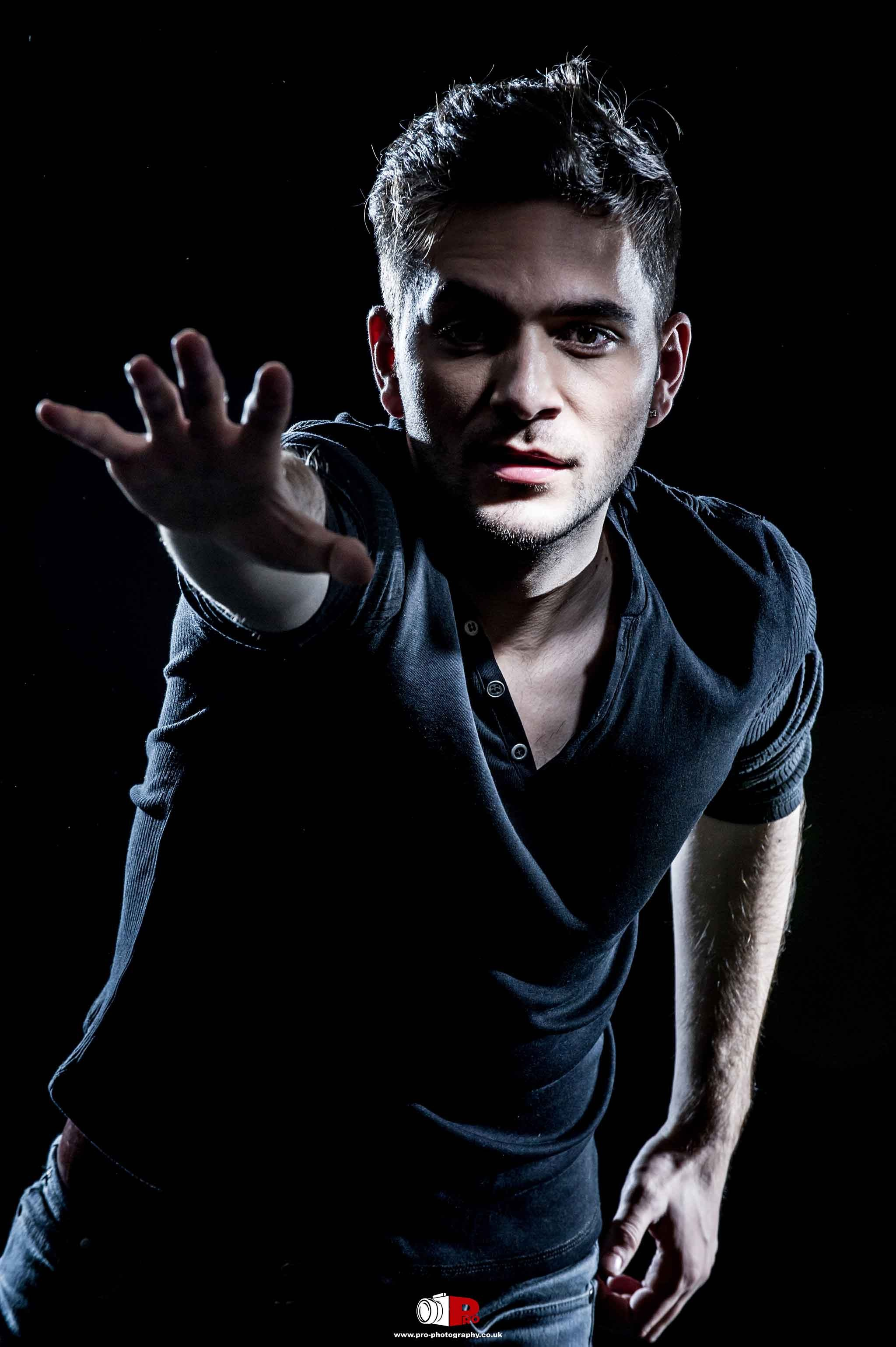 It is an emotional portrait of a man reaching out in a dark setting, showcasing powerful studio lighting and expression.