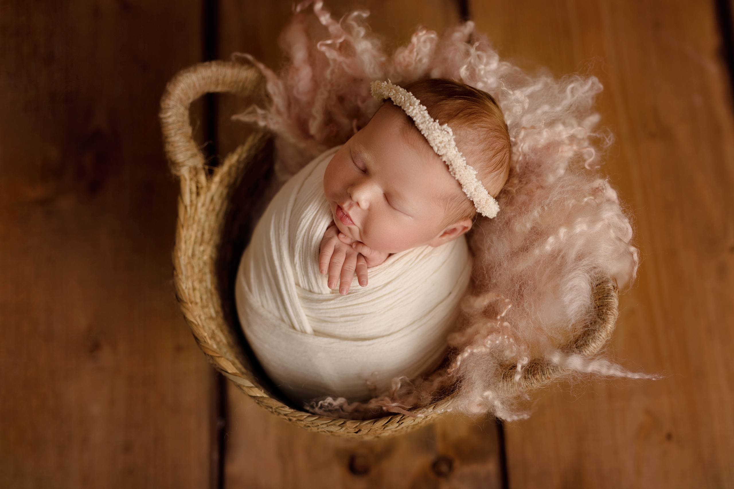 Frisch geborenes Baby eingewickelt in eine Decke, liegt in einem rustikalen Körbchen – Newbornfotografie in Iserlohn