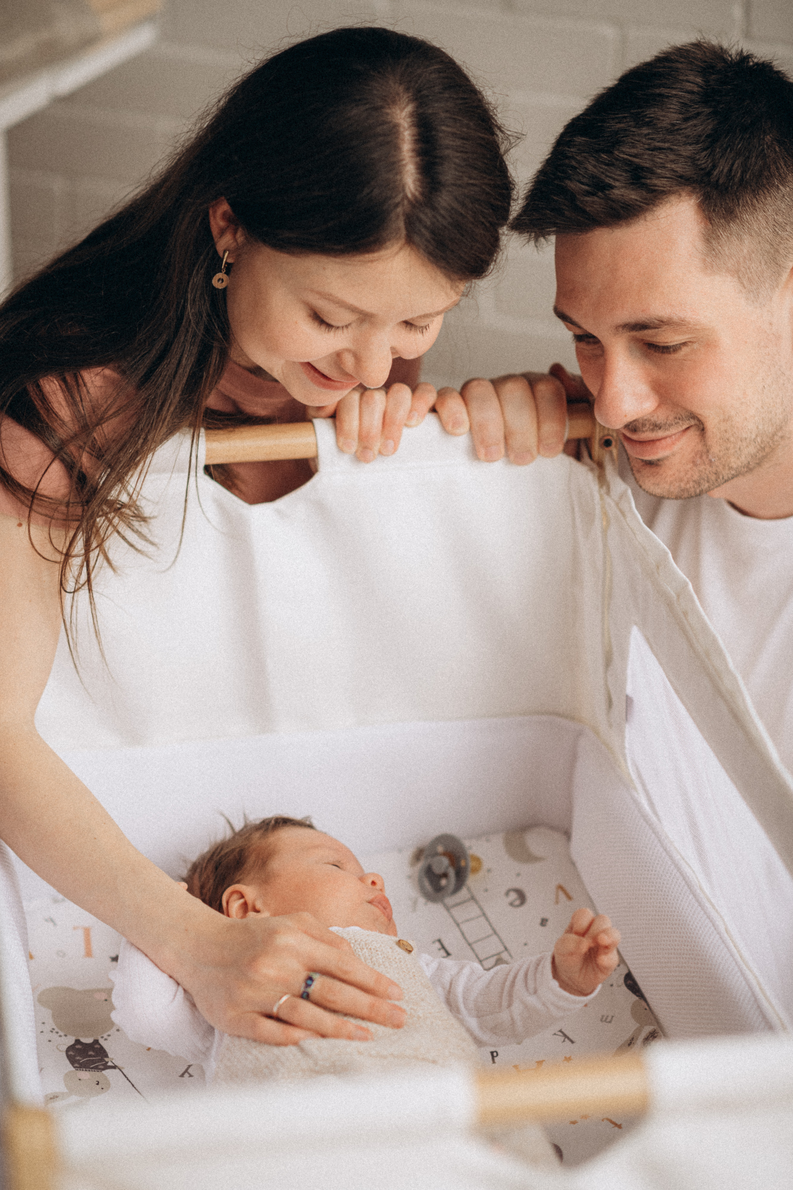 young couple looking at their sleeping baby in the cot