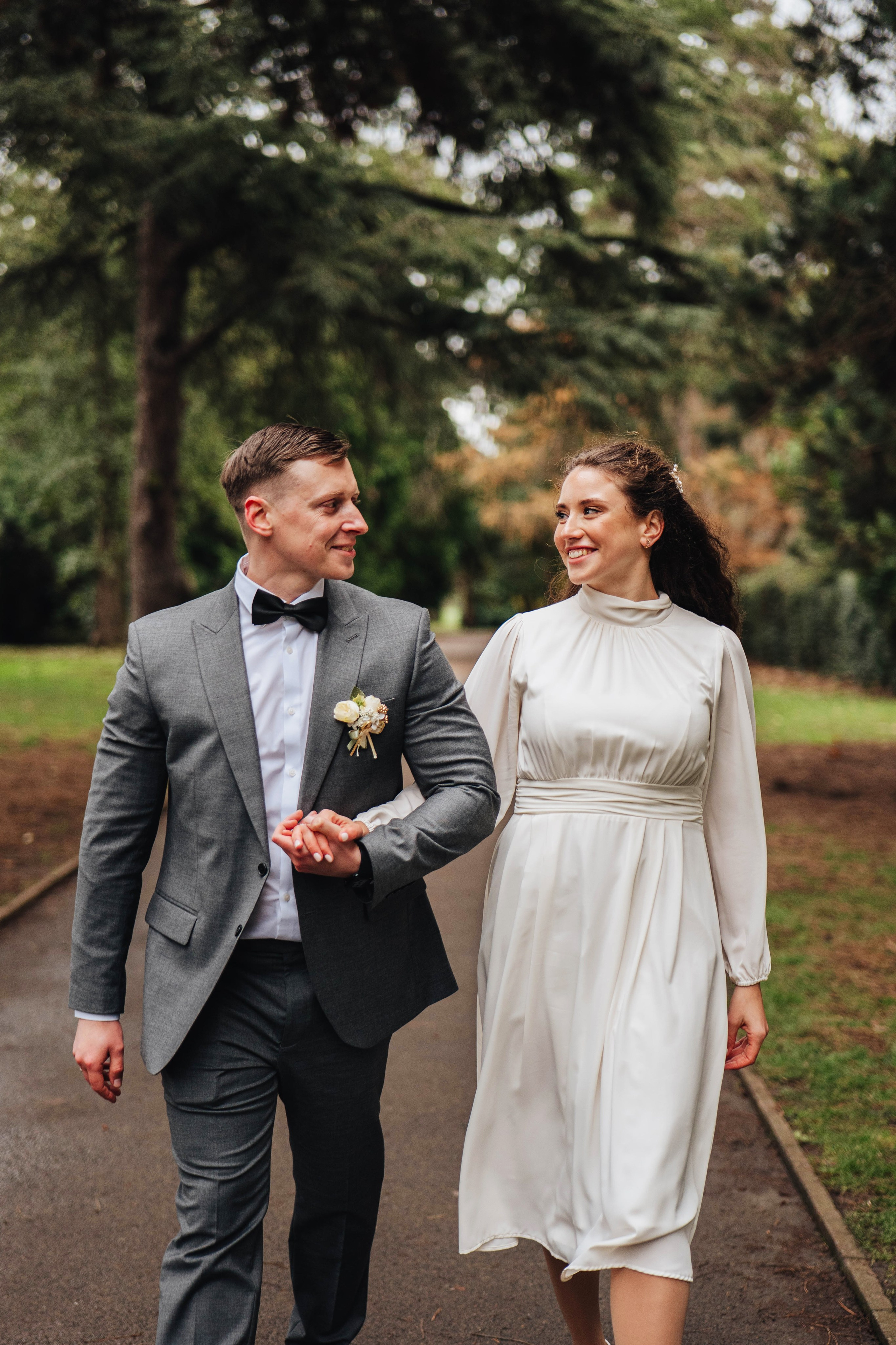 groom and bride walking down the path in the park and smiling at each other