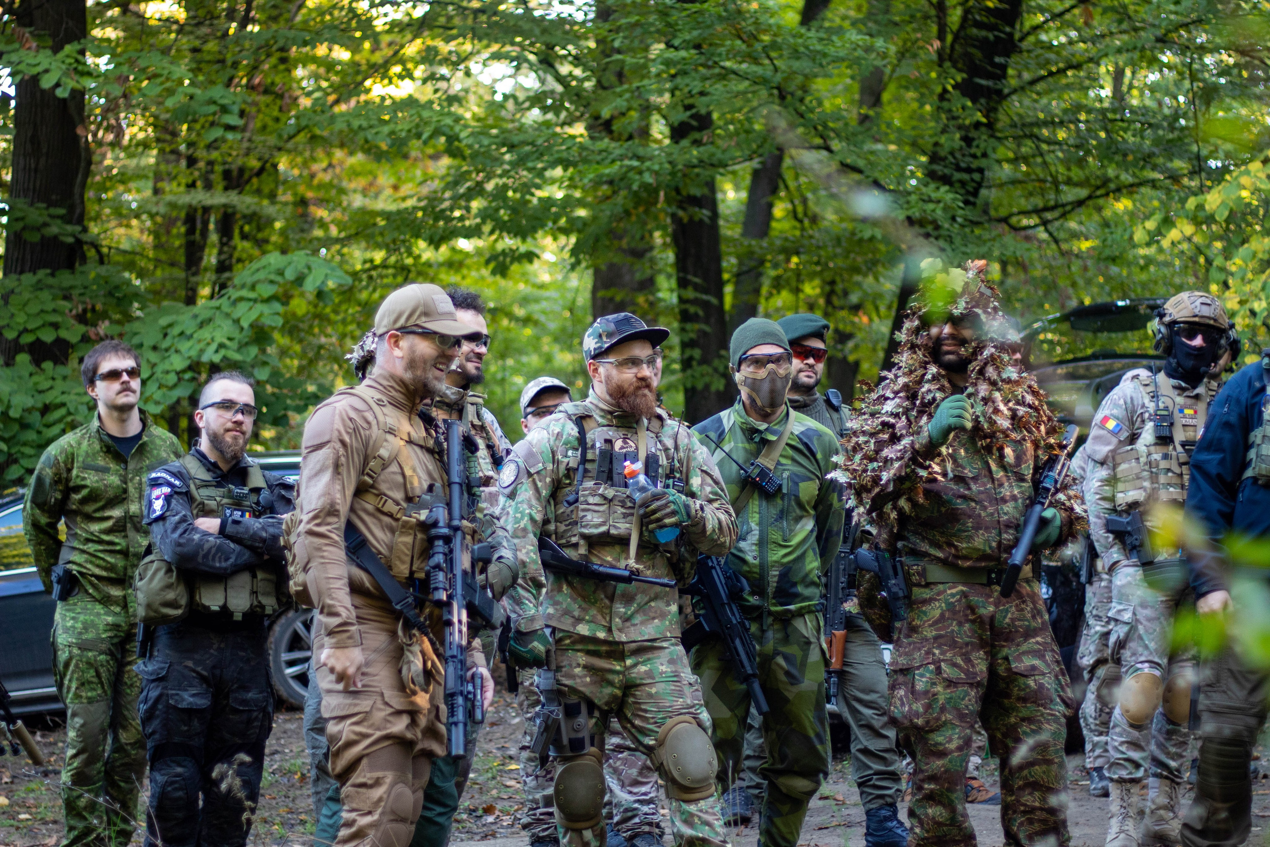 Group of airsoft players in tactical gear standing together in a forest clearing.