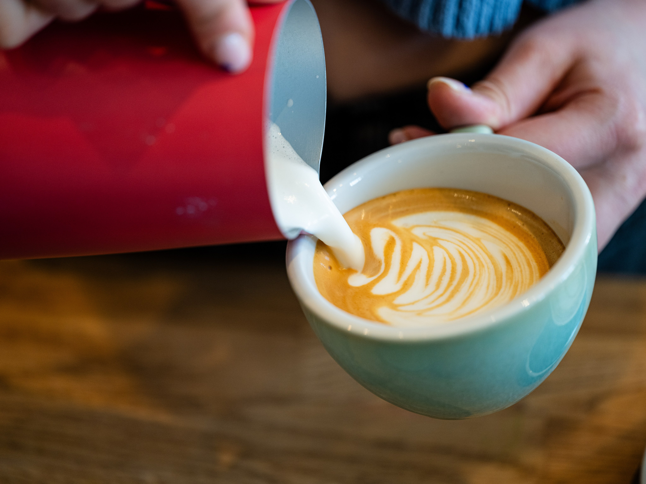 Barista turnând latte art într-o ceașcă de cafea – imagine comercială cu vibe urban, potrivită pentru cafenele artizanale