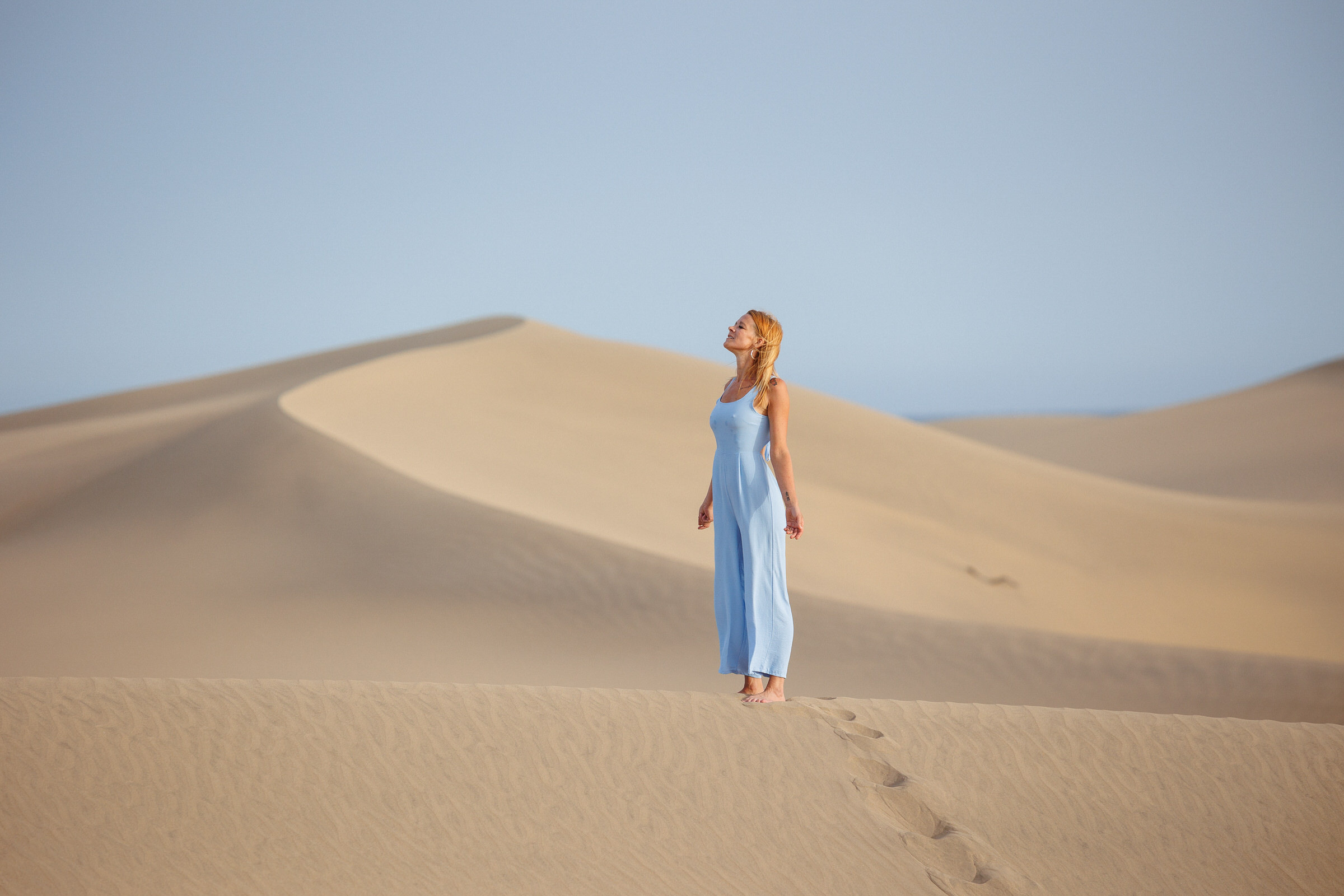A woman in a blue dress stands on a sand dunes in Maspalomas with a professional photographer