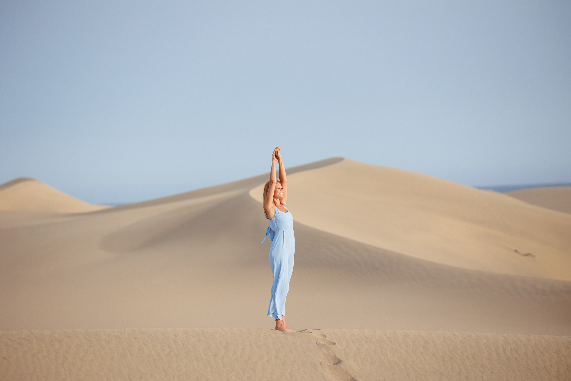A photographer captures a woman in a blue dress standing on a sand dune in the desert of Maspalomas.