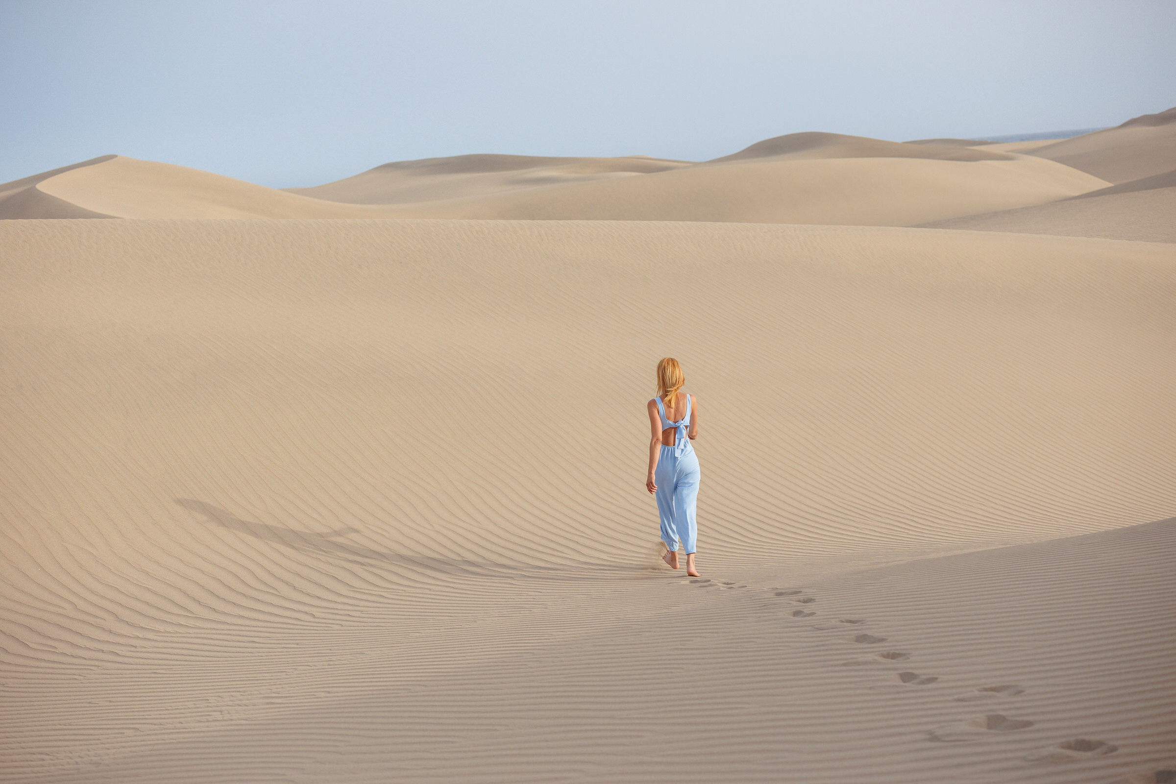 A woman is walking through the Maspalomas sand dunes in a blue dress. With a professional photographer