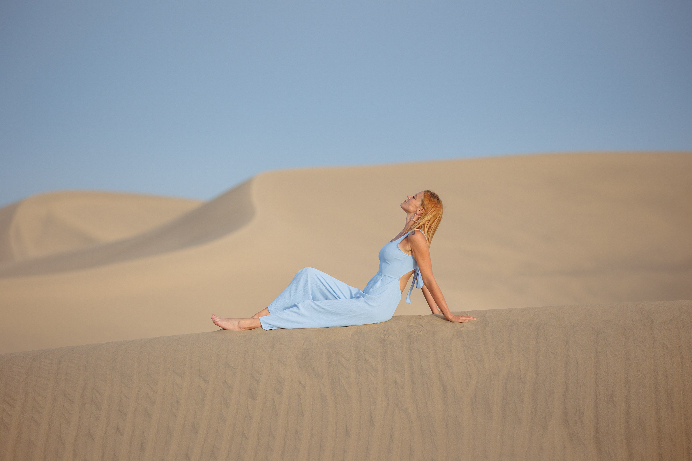 A woman in a blue dress sits on the sand dunes of Maspalomas photo shoot