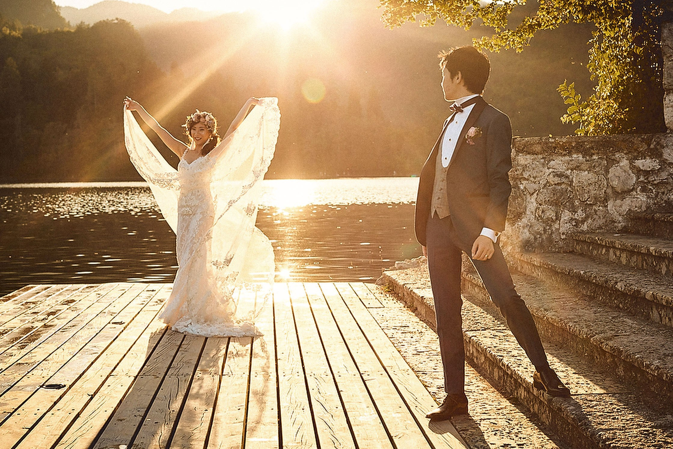 As the golden sunlight flares vividly behind them, a Japanese bride holds up her veil creating a beautiful Angelic pose.