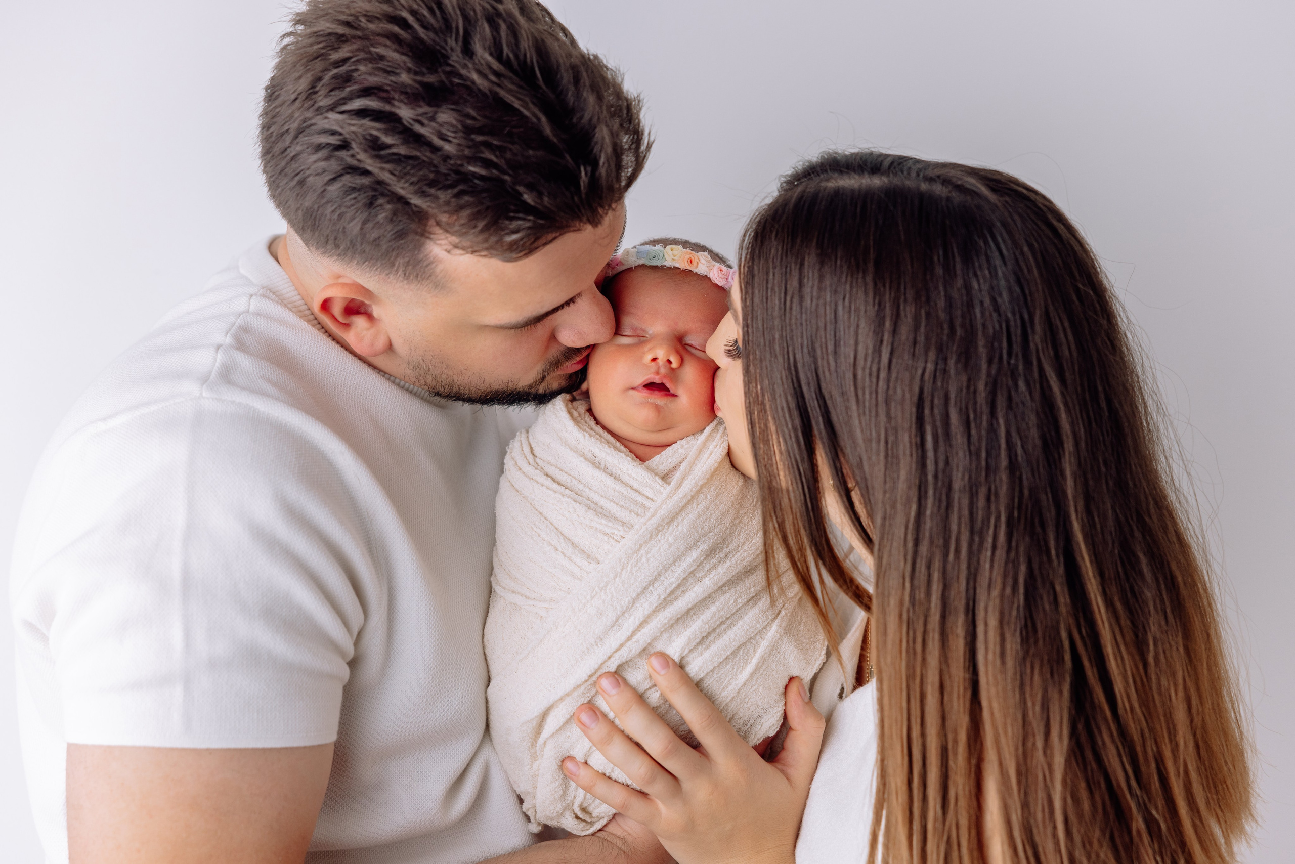 Baby schläft friedlich in den Armen der Mutter und des Vaters – weiches Licht, ruhige Atmosphäre