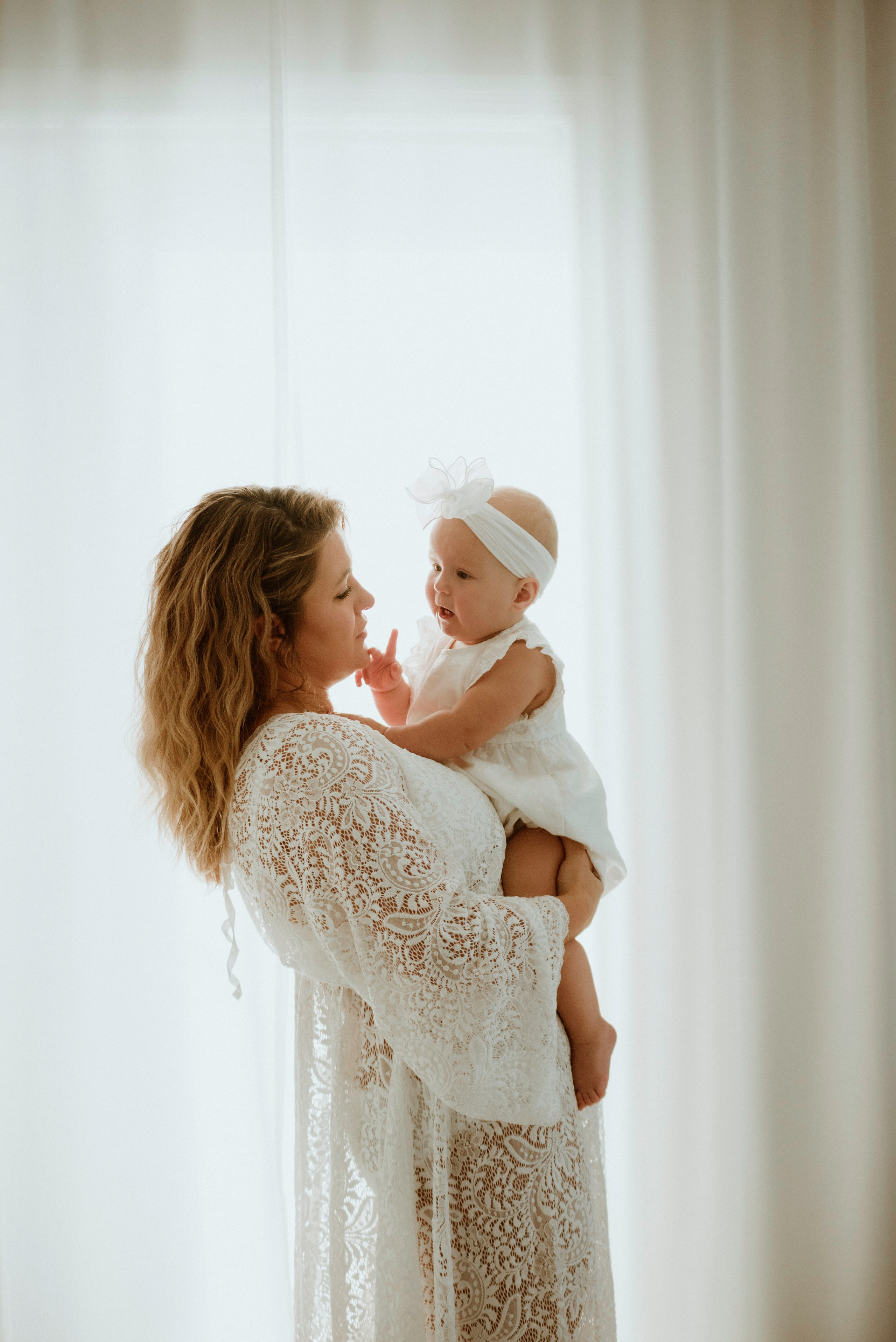 An enchanting outdoor maternity photoshoot at the client's house. The image features a radiant mother and her daughter, both elegantly dressed in white, against the backdrop of their home. The simplicity of their attire and the natural surroundings creates a timeless and intimate atmosphere. Book a personalized outdoor session with MD Studio to capture beautiful moments in the comfort of your own home
