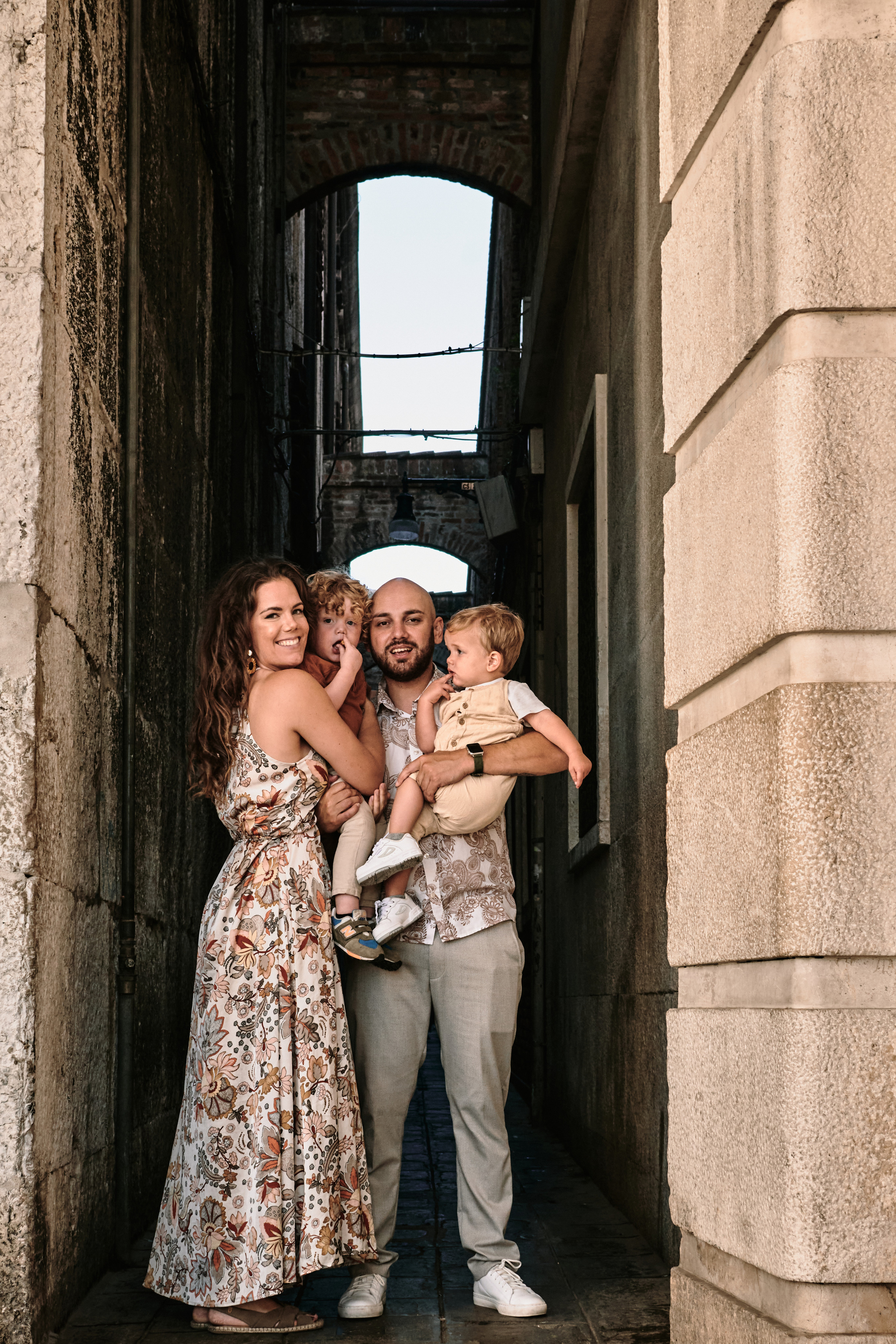 A proud father carries his youngest child on his shoulders as the rest of the family walks along a picturesque Venetian canal, lined with quaint houses and cafes.