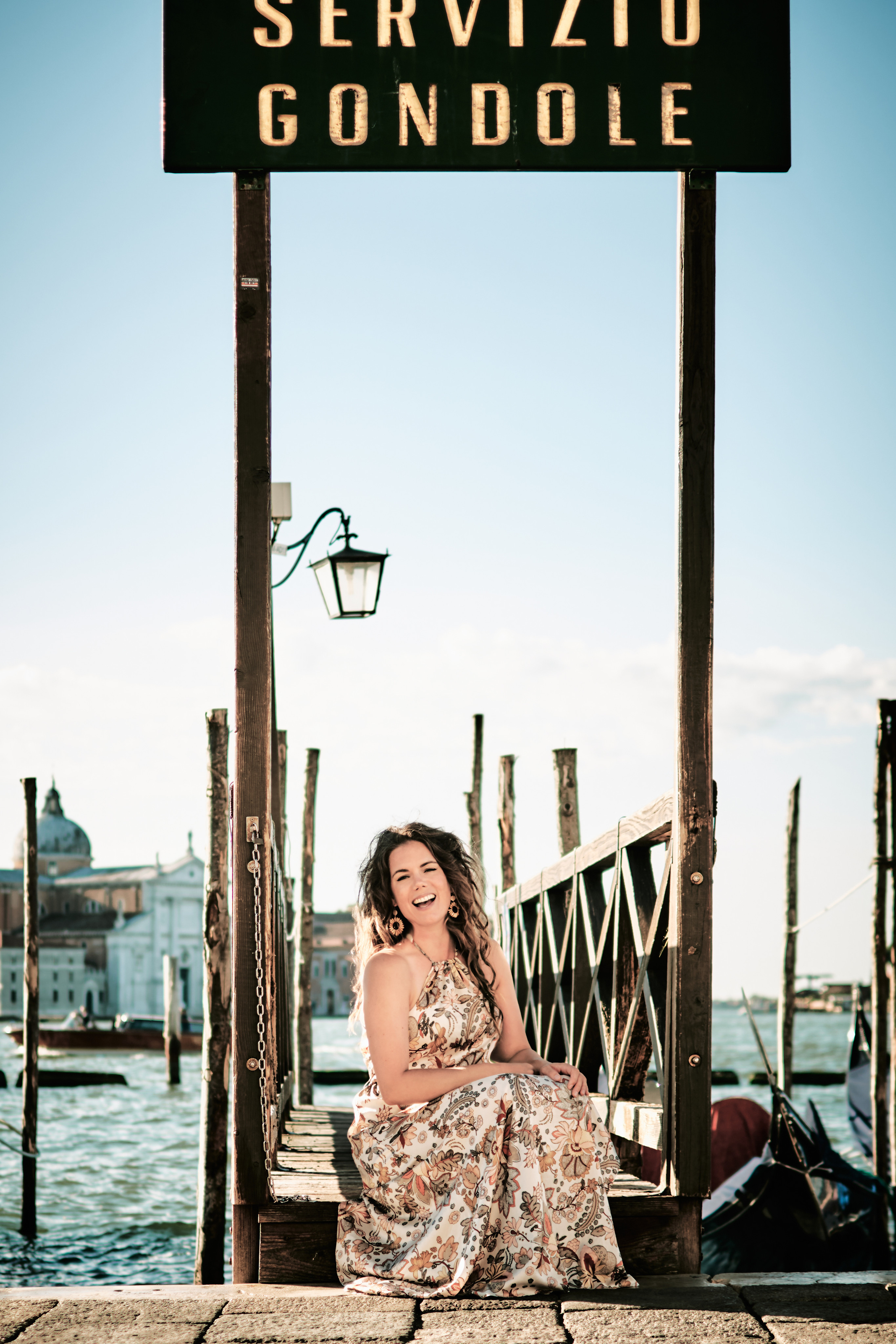 A joyful family stands together on the bustling cobblestone square of San Marco in Venice. In the background, the towering Campanile and ornate Basilica di San Marco are visible, surrounded by bustling cafes and souvenir shops. The warm glow of the sun casts a golden light over the scene, highlighting the family's smiling faces and the colorful buildings that line the square."