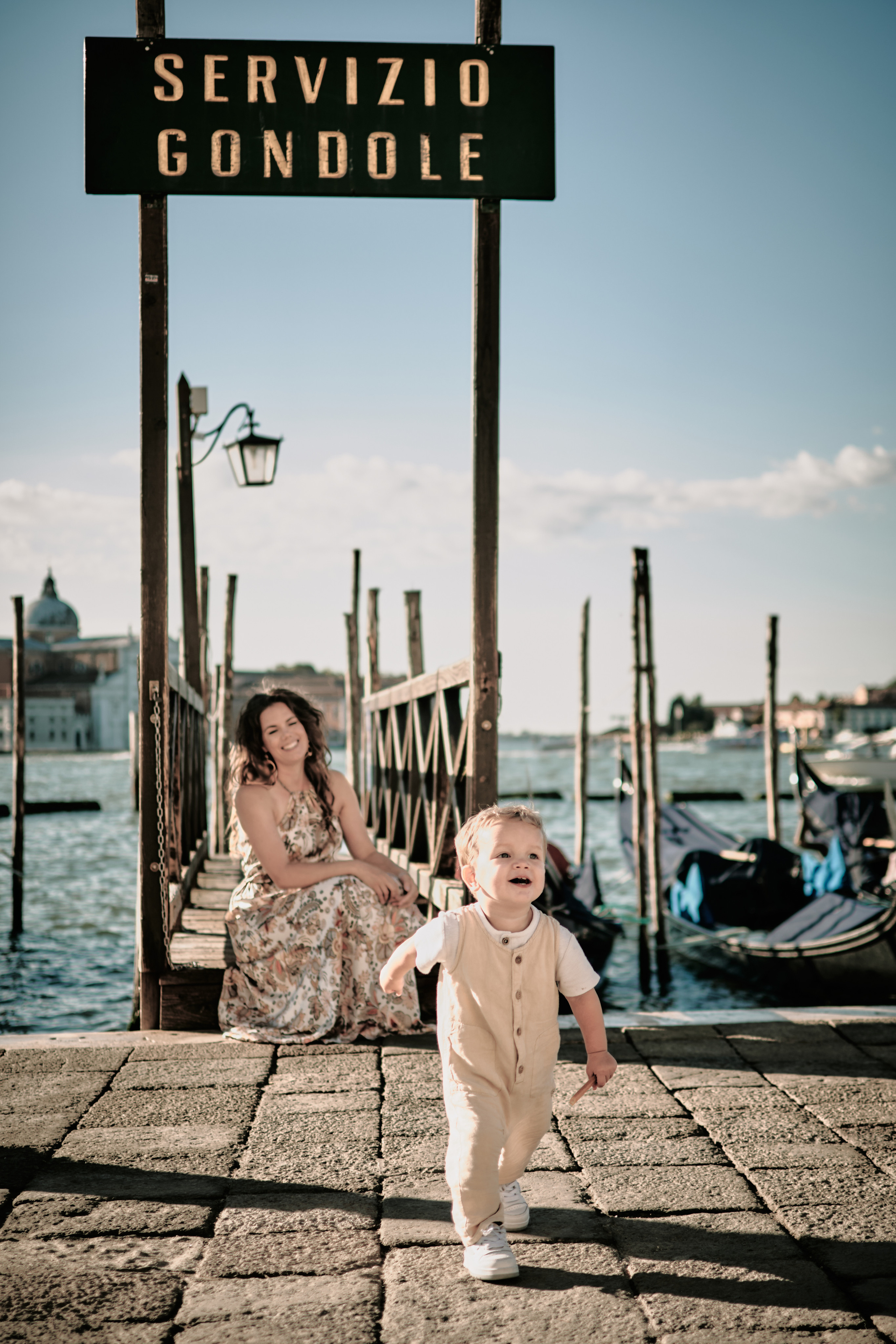 A happy family of four standing on a bridge over a canal in Venice, Italy, with the iconic gondolas in the background.
