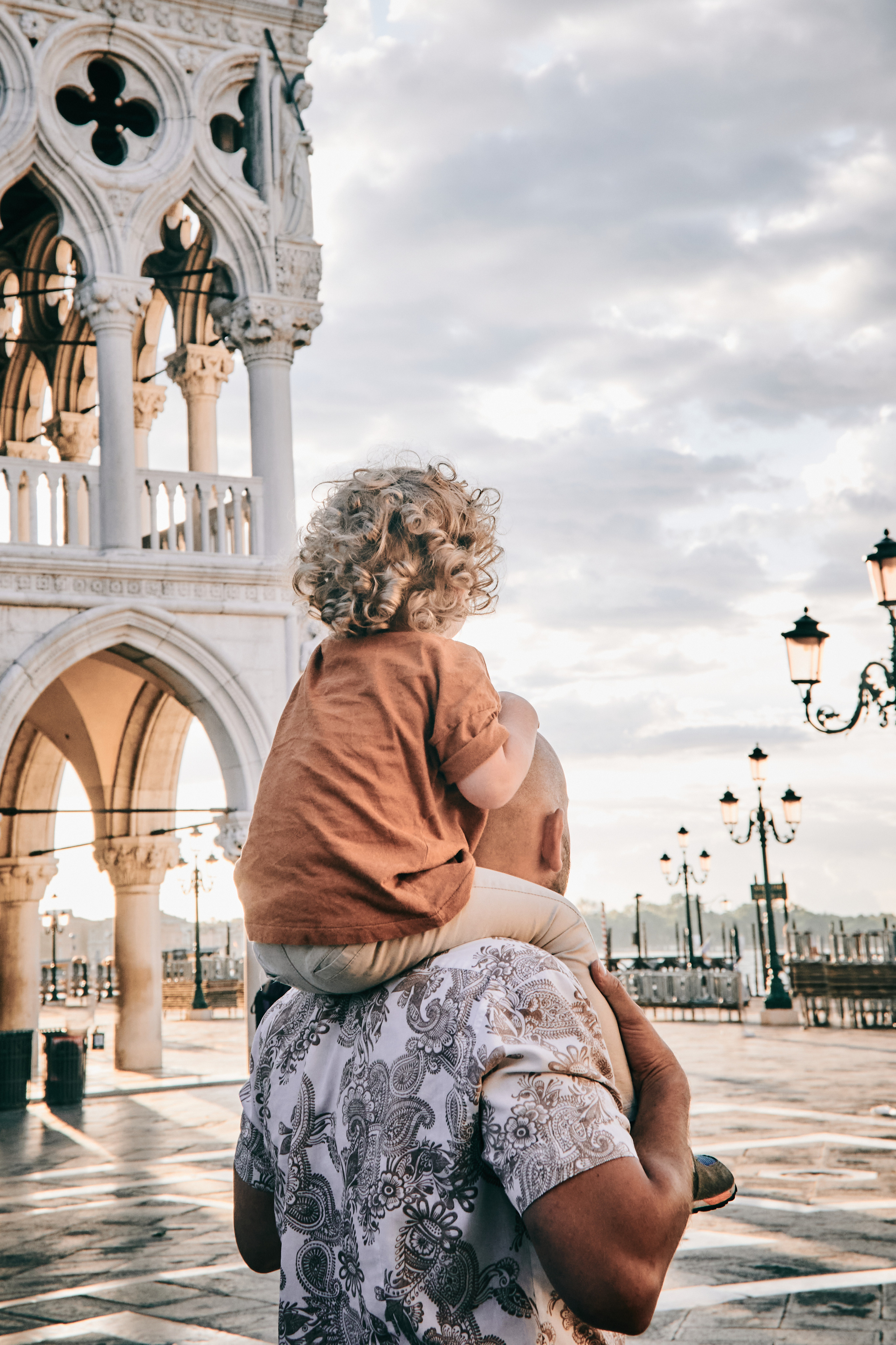 This family photo captures a beautiful moment on San Marco Square in Venice. The dad stand with his child, all of them looking joyful and content. In the background, the grandeur of Venice's architecture can be seen, adding to the beauty of the scene.