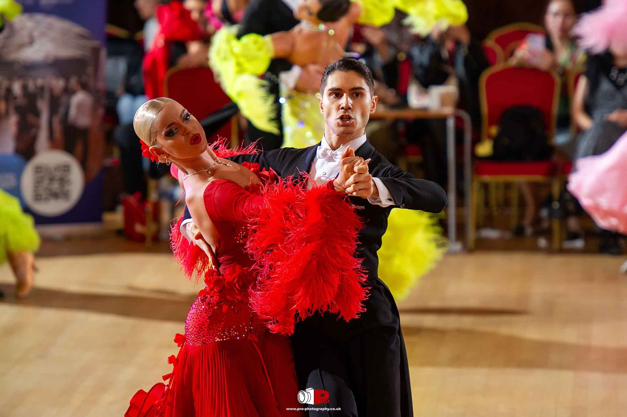 Male and female ballroom dancers in a stunning red and black performance with bright feathers and synchronized movements.