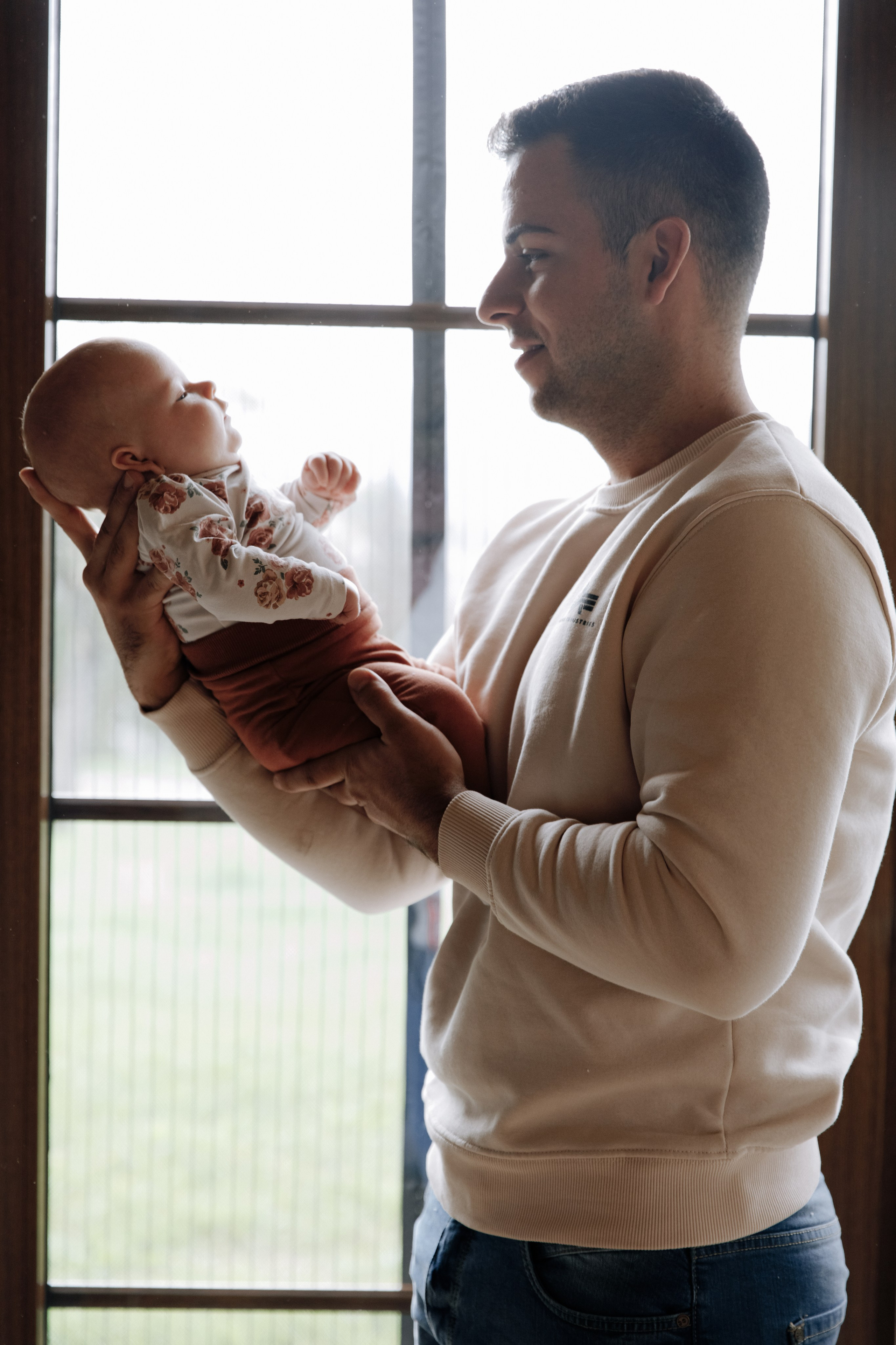 Vater steht am Fenster und hält seine kleine Tochter im Arm.