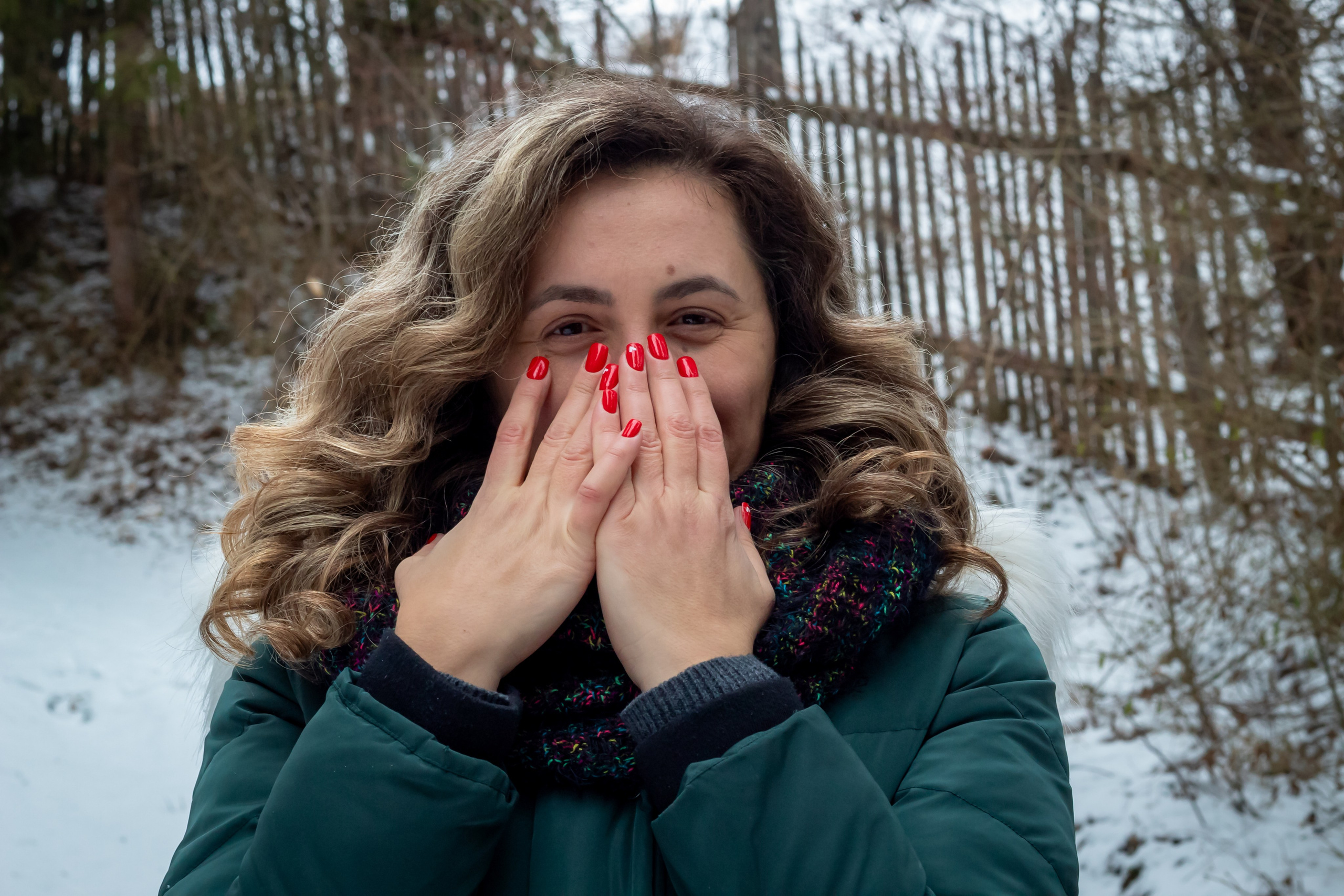 Woman in winter coat and gloves smiling while standing in a snowy outdoor setting.
