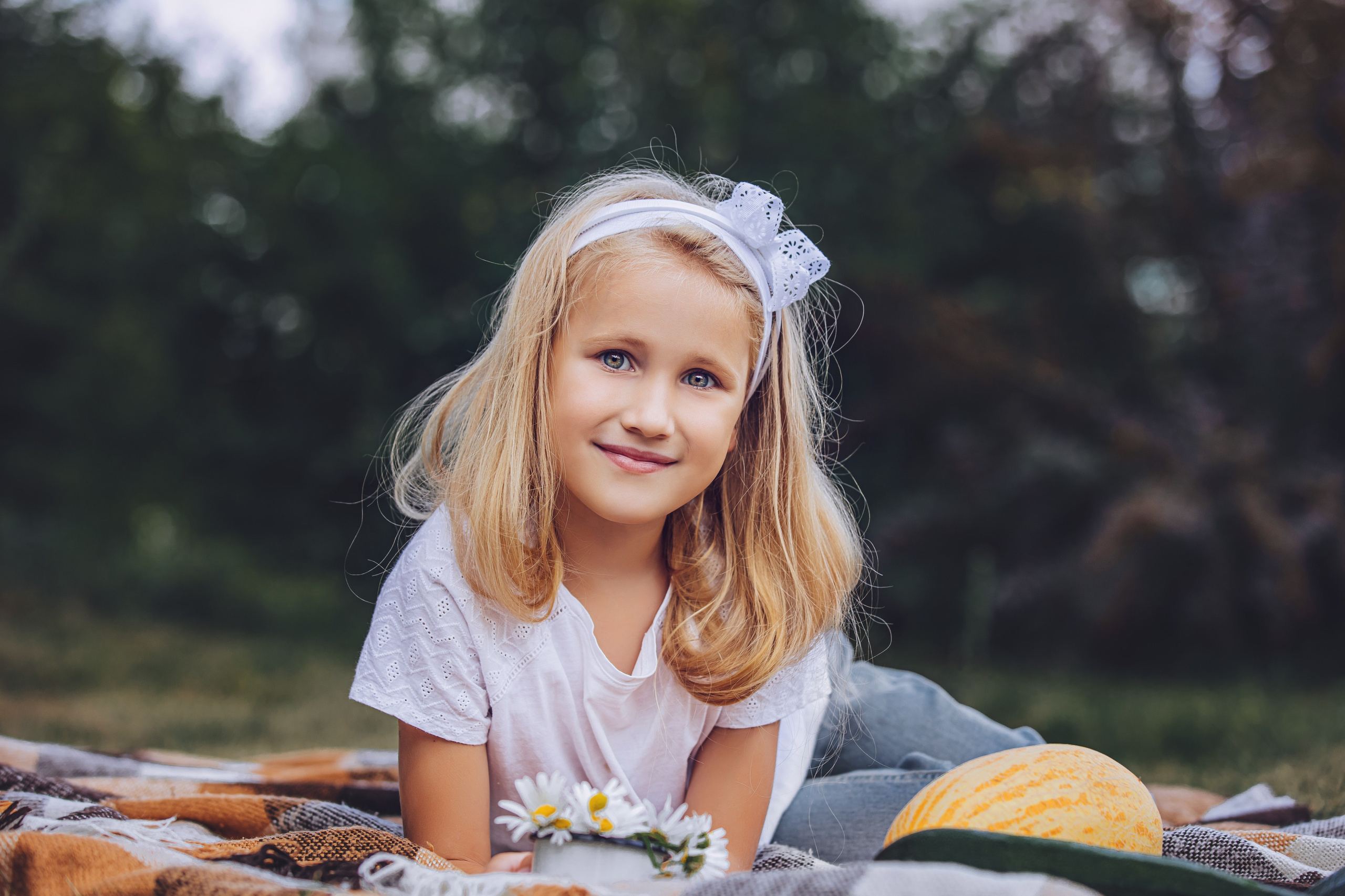 Petite fille blonde avec un nœud allongée sur une couverture de pique-nique, sourire joyeux