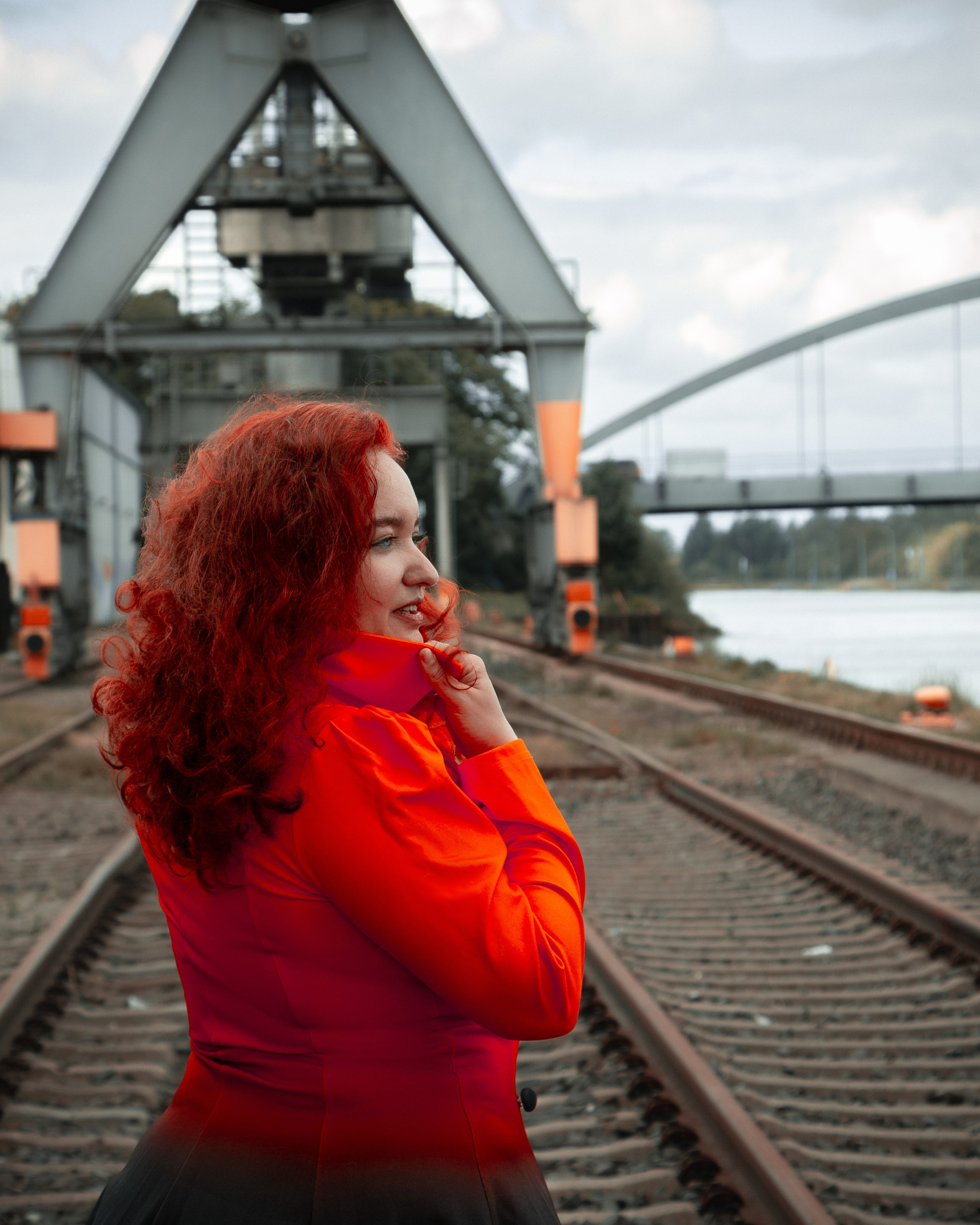 Ksenia mit leuchtend roten Haaren in feurigem Kleid auf urbanem Industriehintergrund