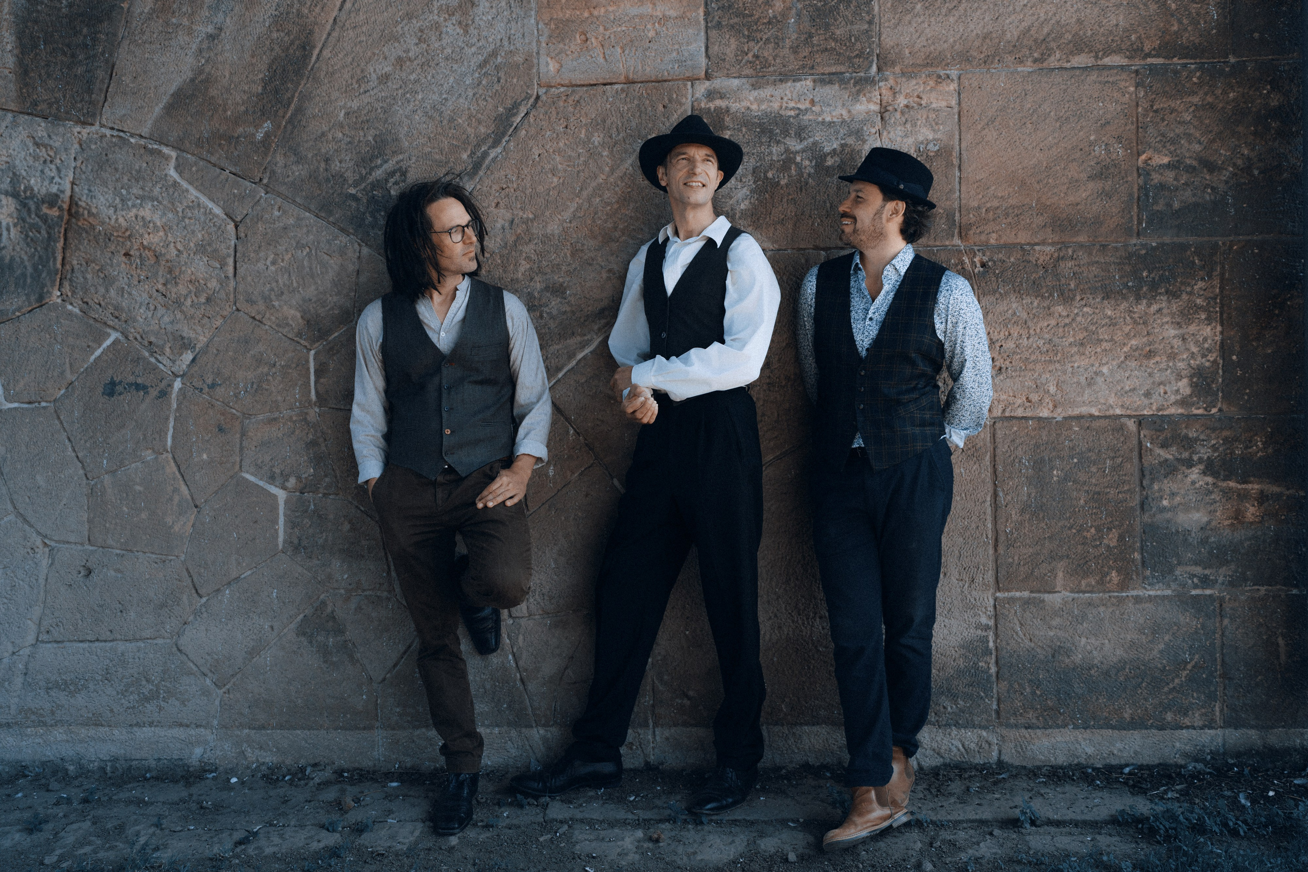 Drei Musiker der Band Ziganimo lehnen entspannt an einer Steinwand
