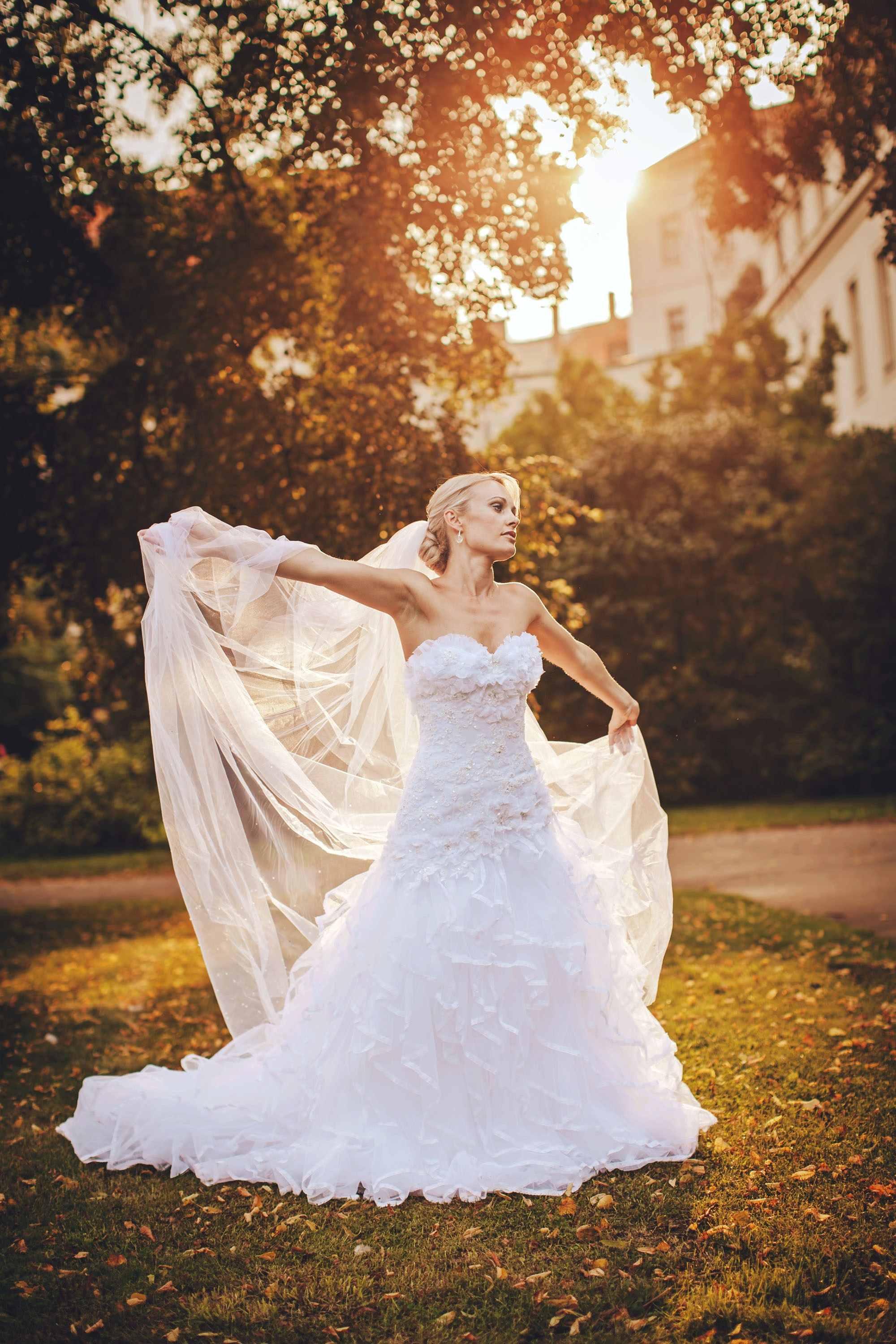 New Zealand blonde bride adjusting veil at sunset in a golden Prague garden.