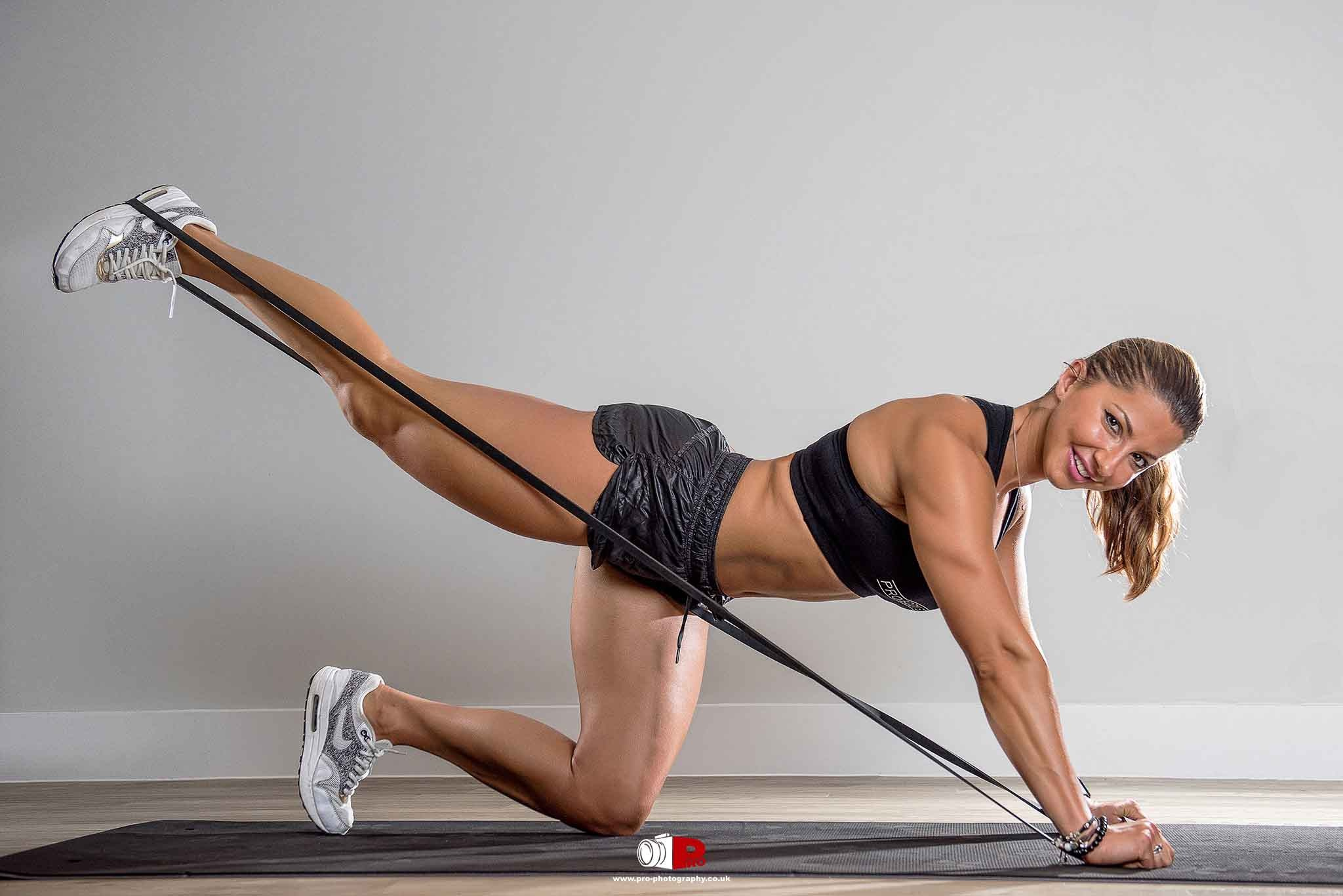 A fit woman smiling while performing a resistance band workout on a yoga mat, engaging her glutes and core.