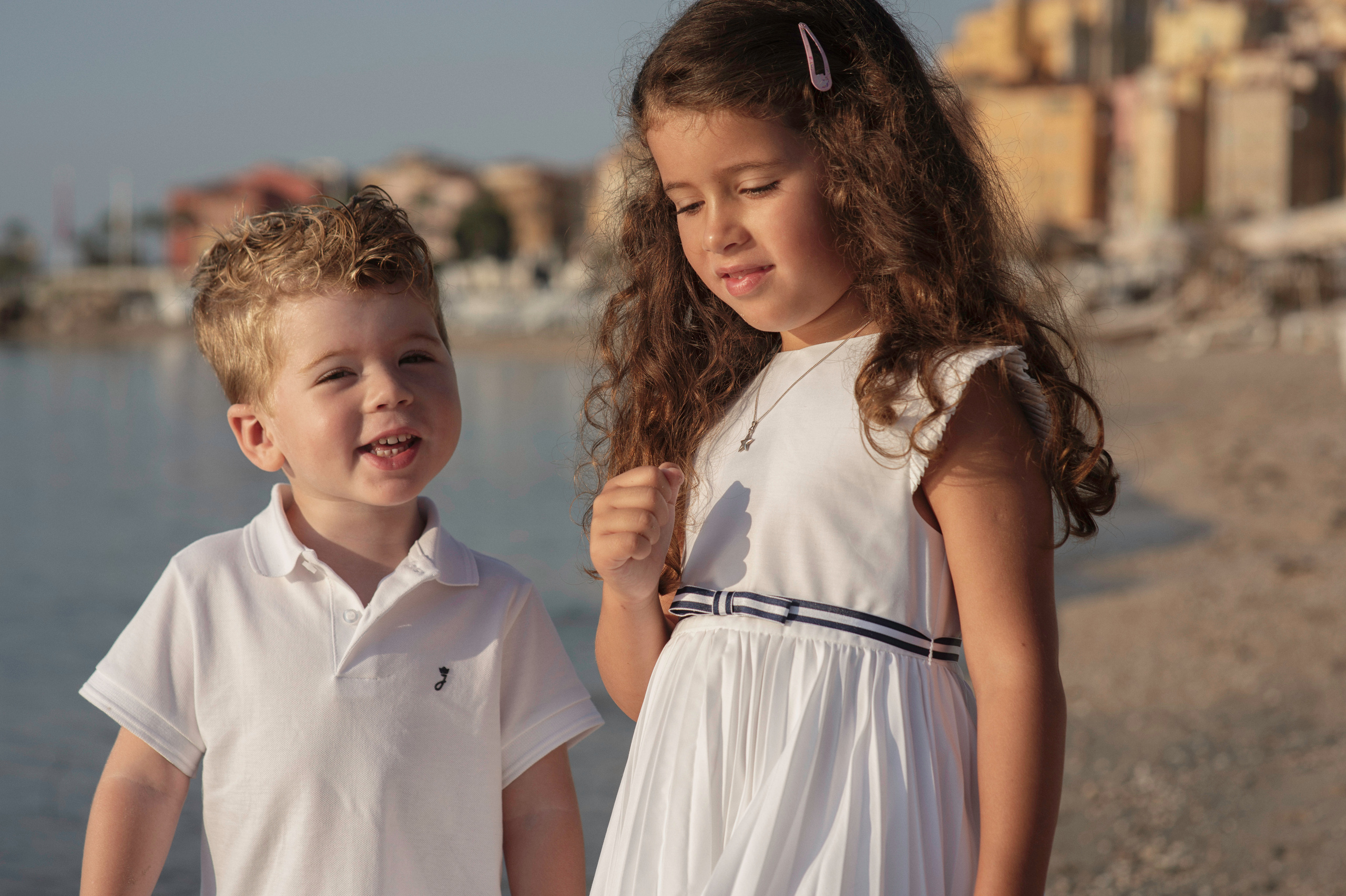 Un frère et une sœur se tiennent par la main en marchant sur la plage.