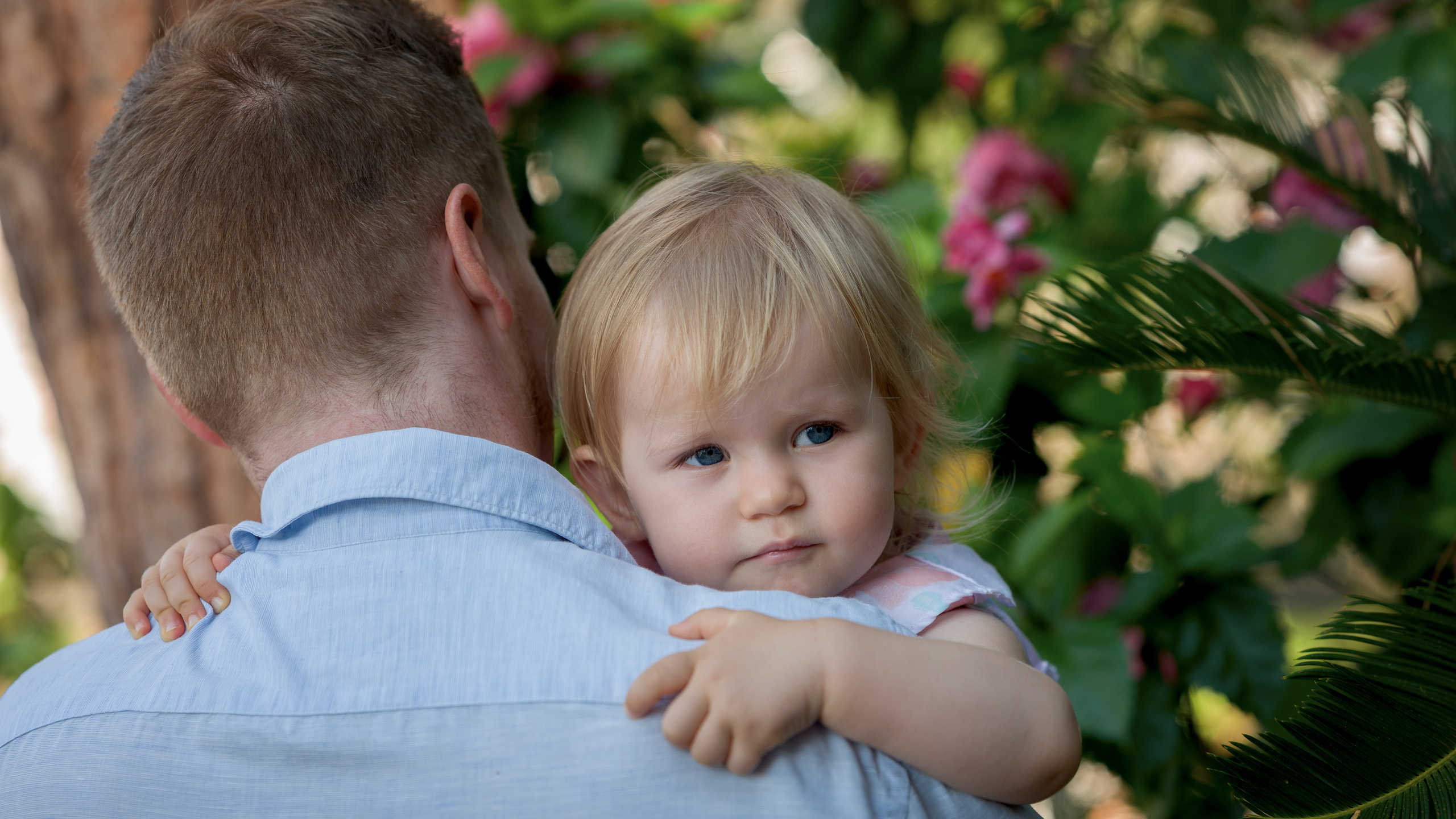 Une fille dans les bras de son père, regardant par-dessus son épaule avec un sourire.