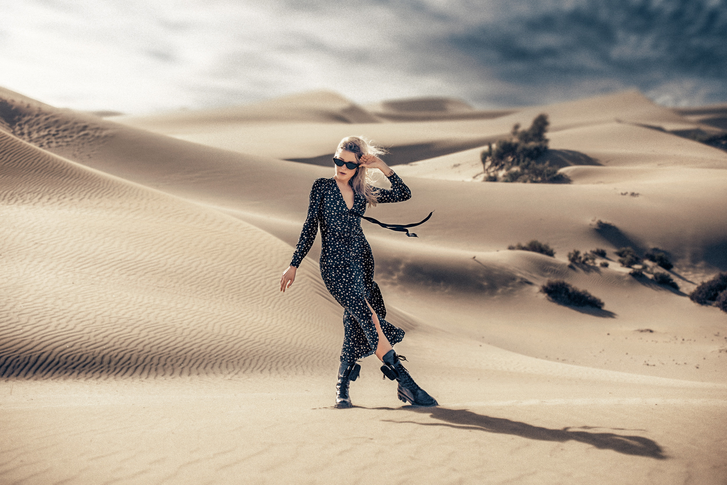 A woman in a black dress walking through the sand dunes.