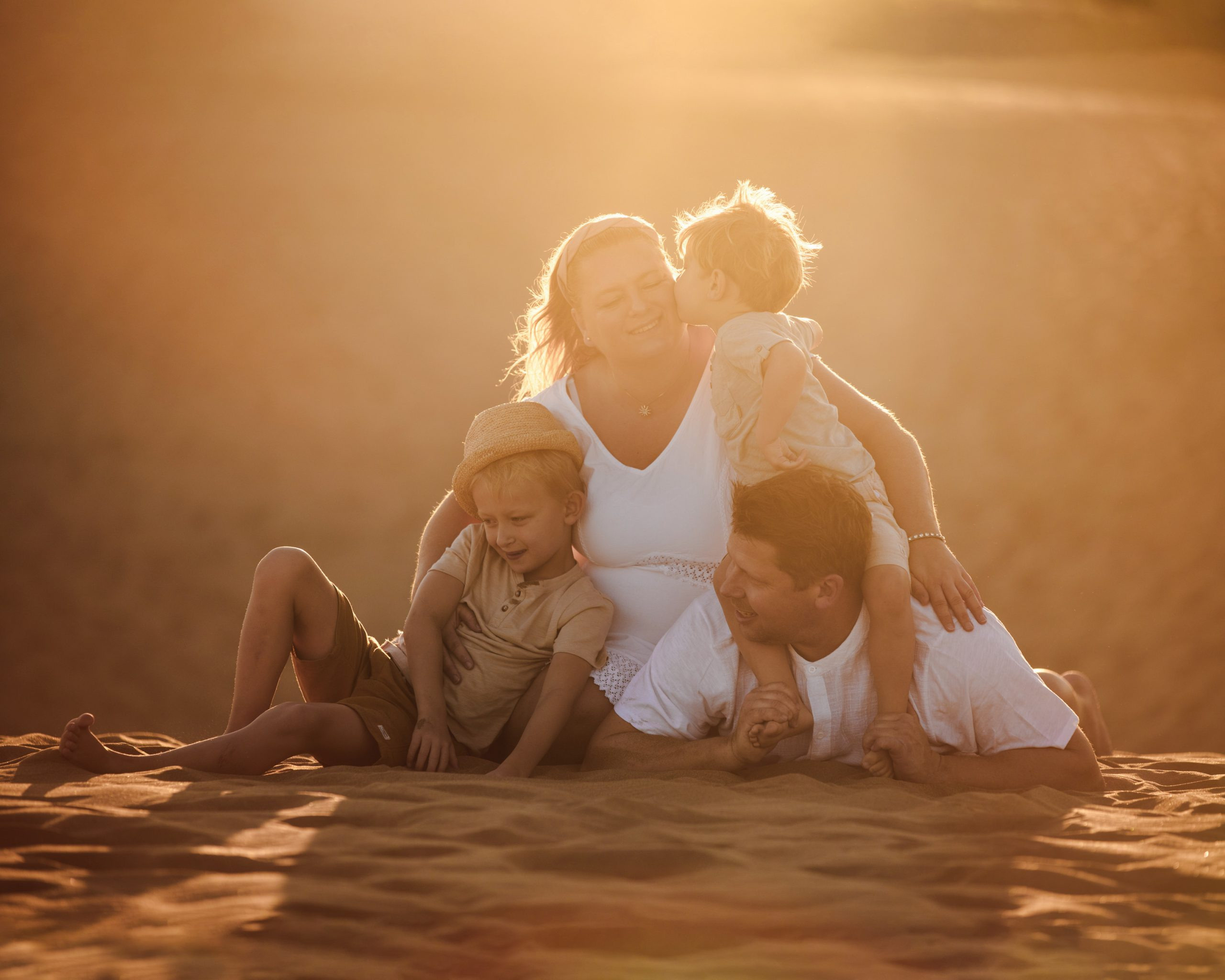 Une famille est assise sur une dune de sable au coucher du soleil.