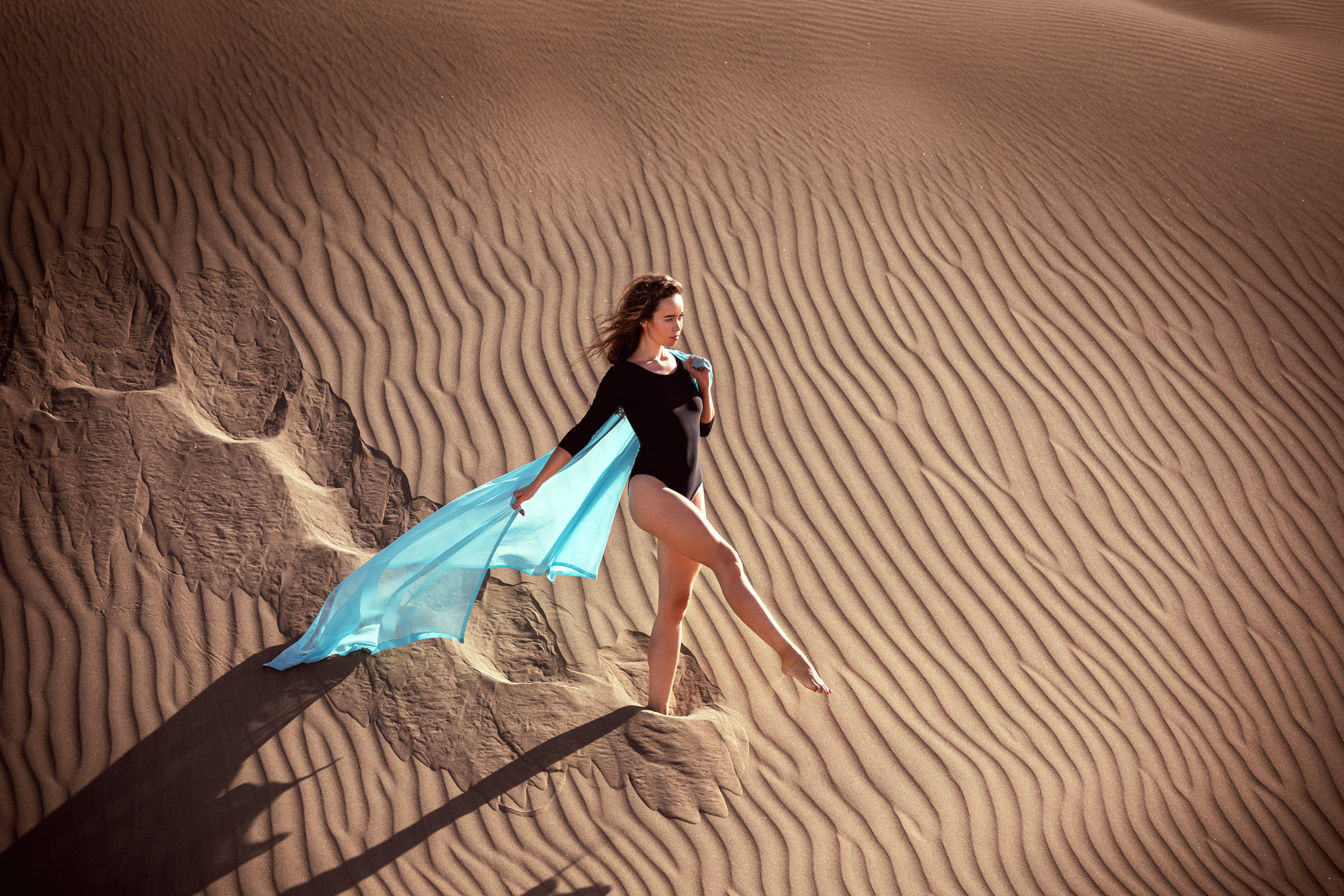 Discover the captivating beauty of a woman in a blue cape against the stunning desert backdrop of Maspalomas through the lens of a talented photographer.