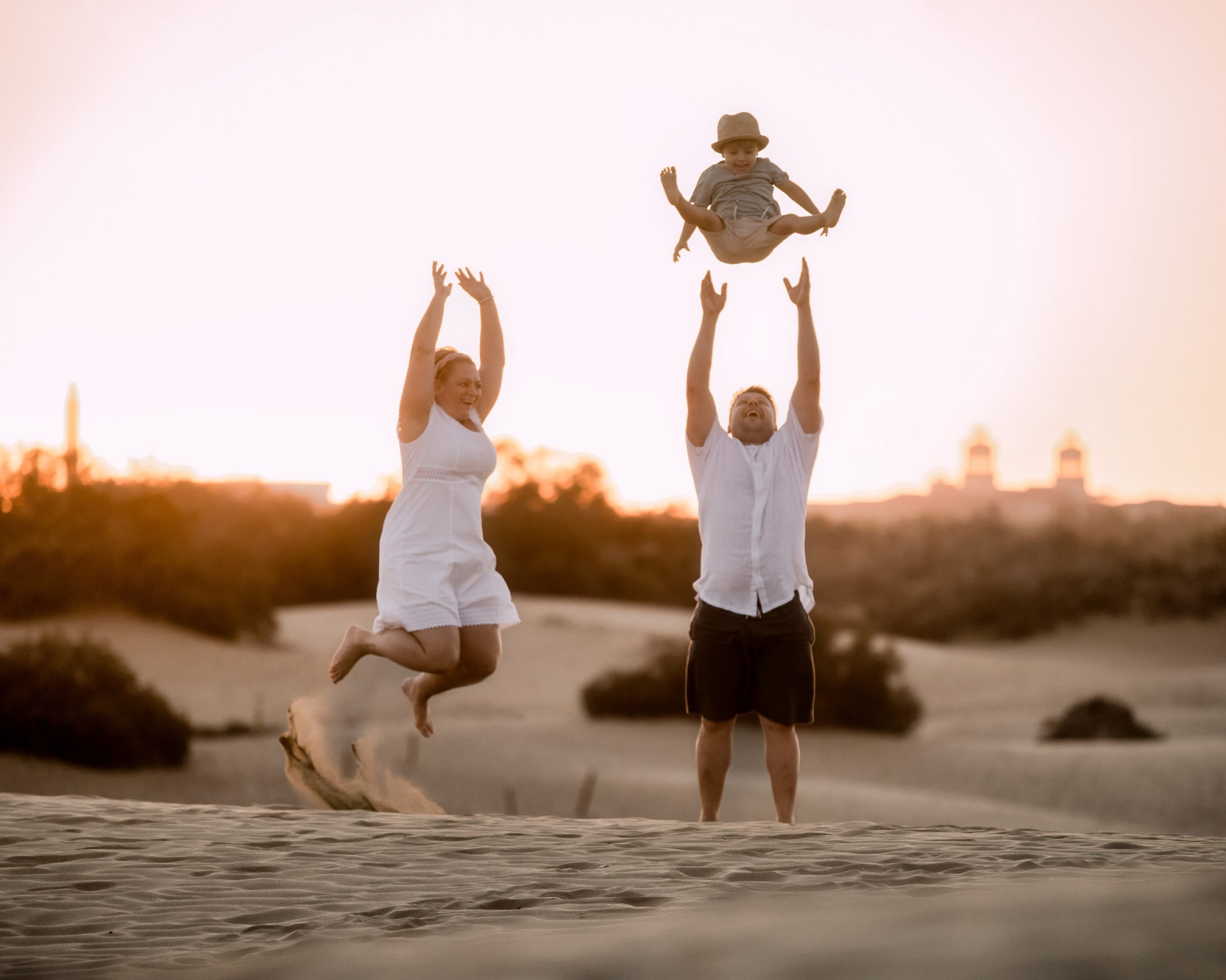Une famille tient son enfant en l'air dans les dunes de sable.
