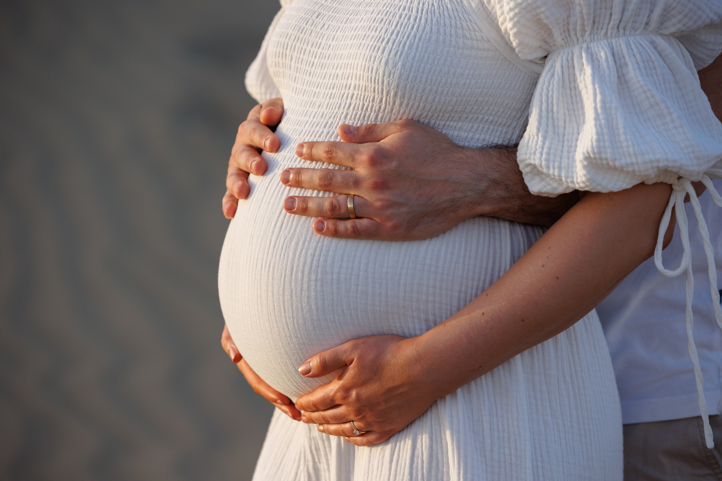 A photographer captures a tender moment as a pregnant woman holds her husband's hand on the sand.