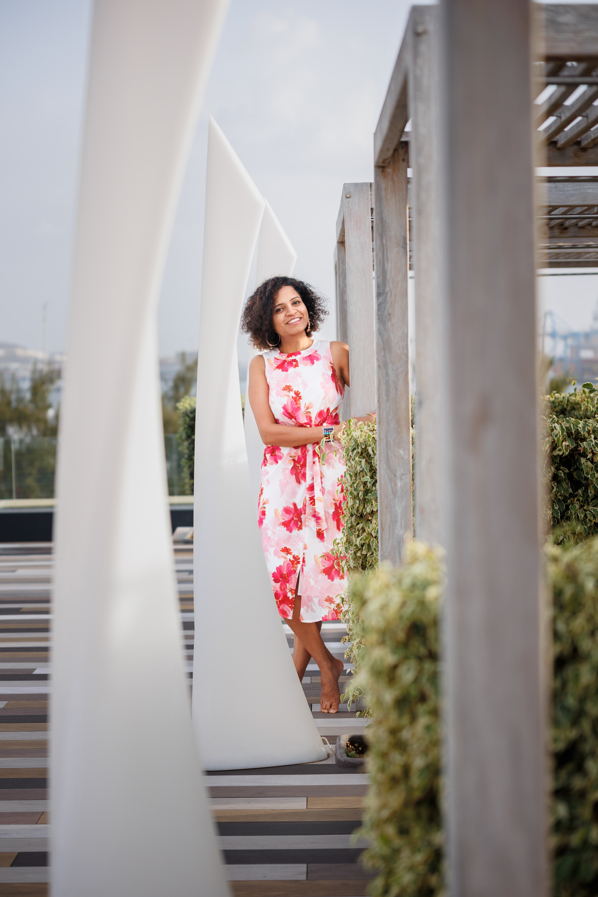 Capture the essence of elegance with our portrait photo shoot in a hotel, featuring a woman in a stunning floral dress leaning against a rustic wooden structure.