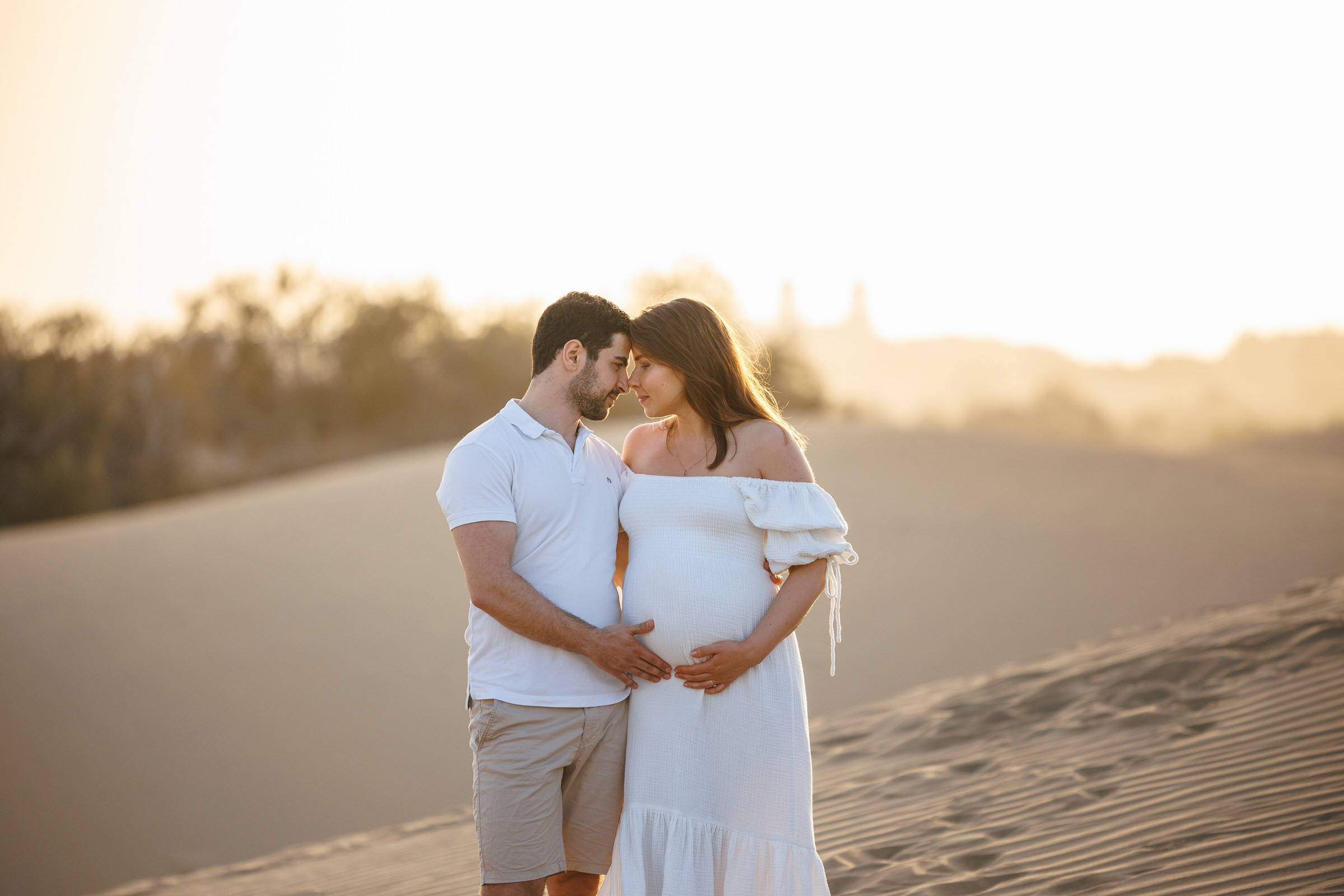A beautiful moment captured by a photographer: a pregnant couple standing in Maspalomas at sunset.