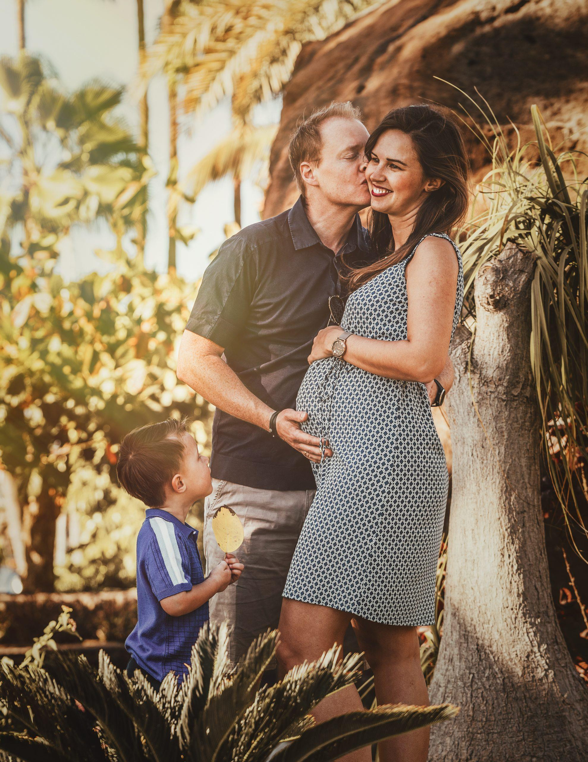 Un couple enceinte s'embrassant devant un palmier