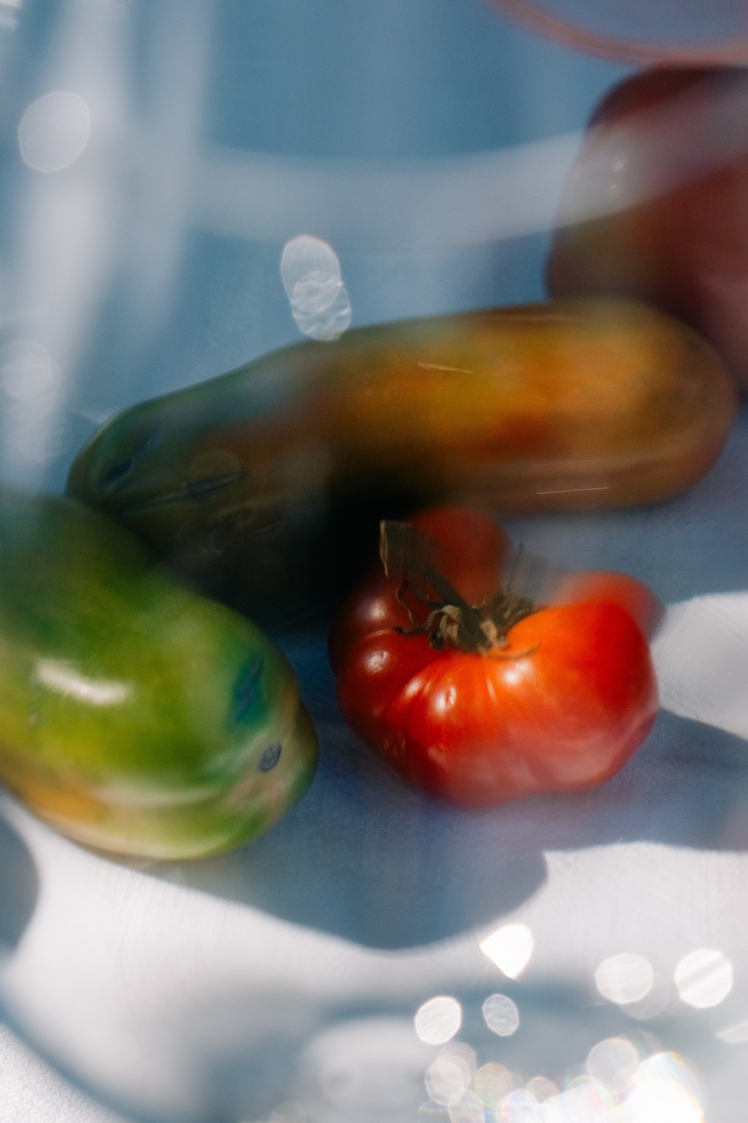 Reflexão abstrata de tomates e pepinos através de vidro. Imagem abstrata de tomates e pepinos distorcida através de uma superfície de vidro com reflexos suaves e reflexos ligeiros.