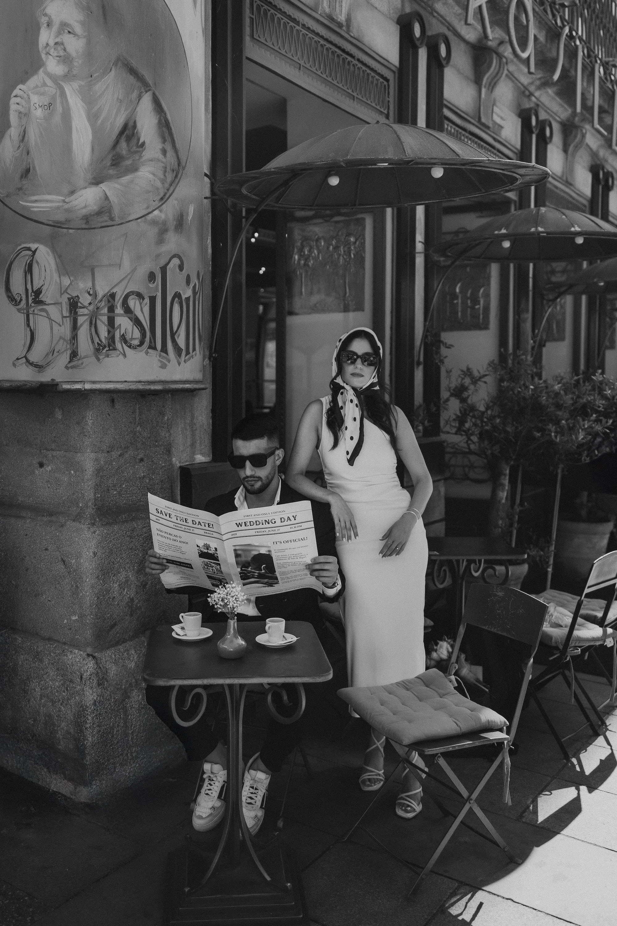 Casal elegante com o noivo a ler jornal enquanto a noiva aguarda numa sessão editorial pré-casamento