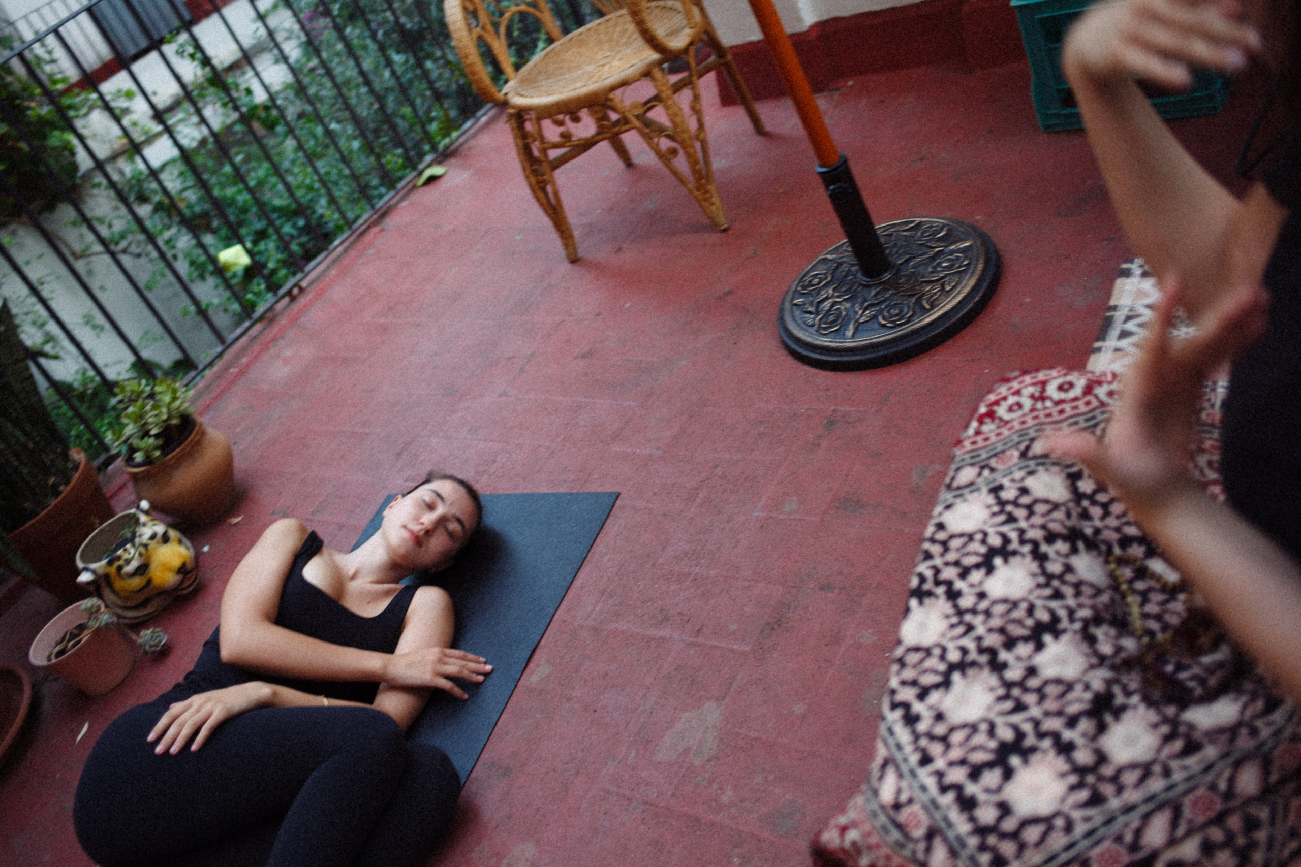 Woman lying and relaxing on a red mat outdoors, surrounded by plants