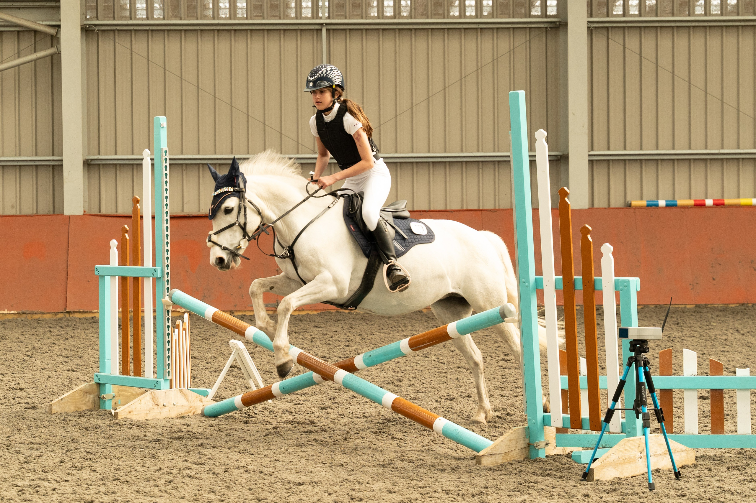 Professional photo of horse and rider over teal and white vertical jump