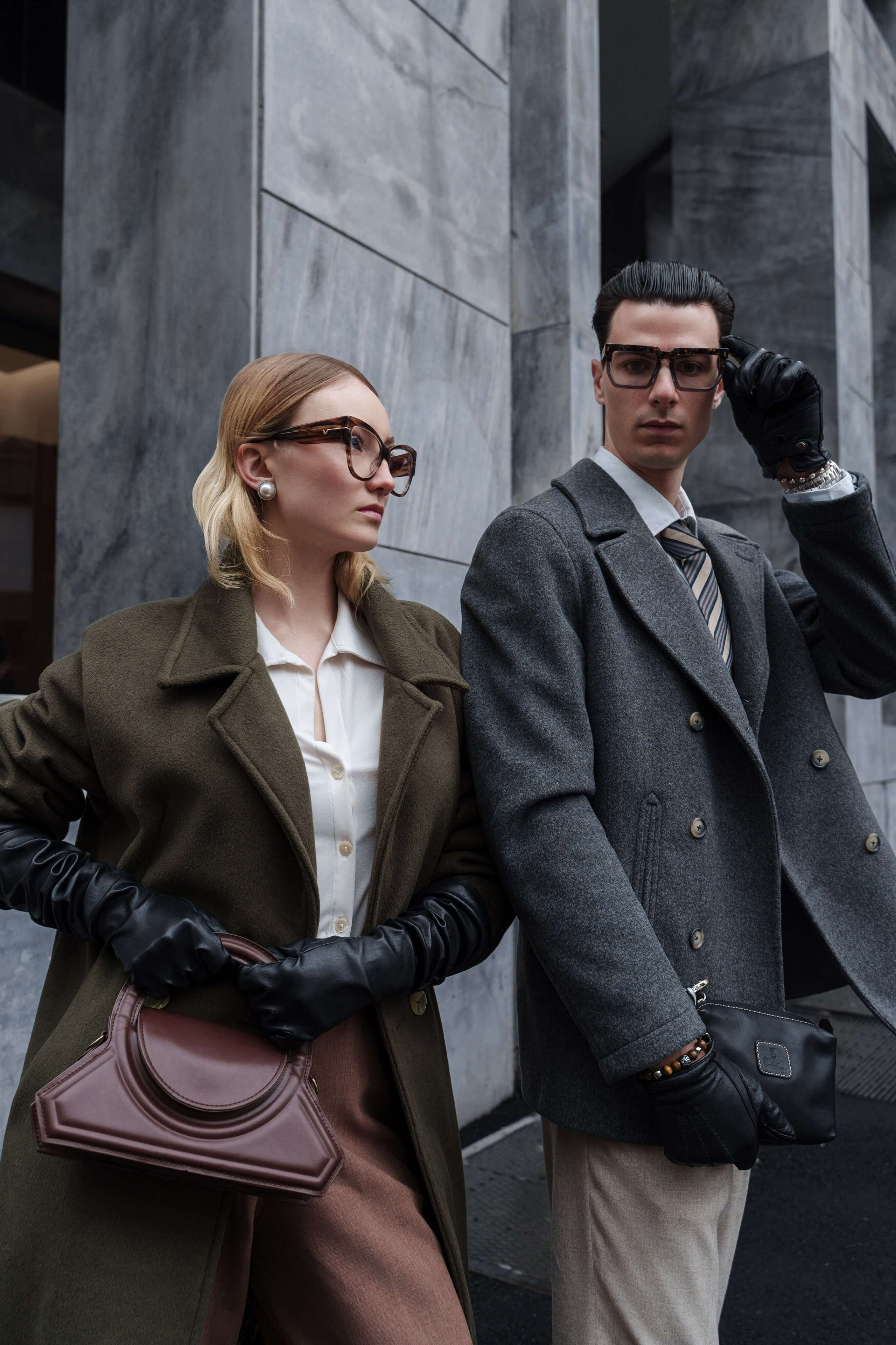 Fashionable man and woman in statement glasses posing against a modern architectural background