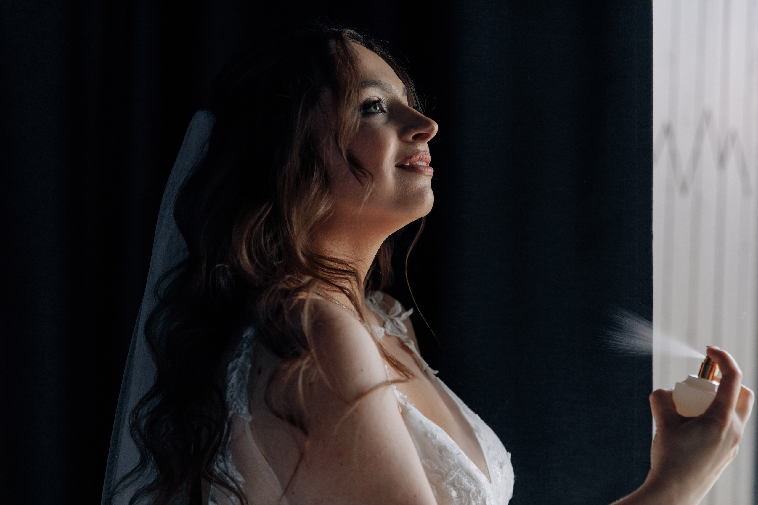 Die Braut sprüht Parfüm, während sie im Profil zu uns steht.